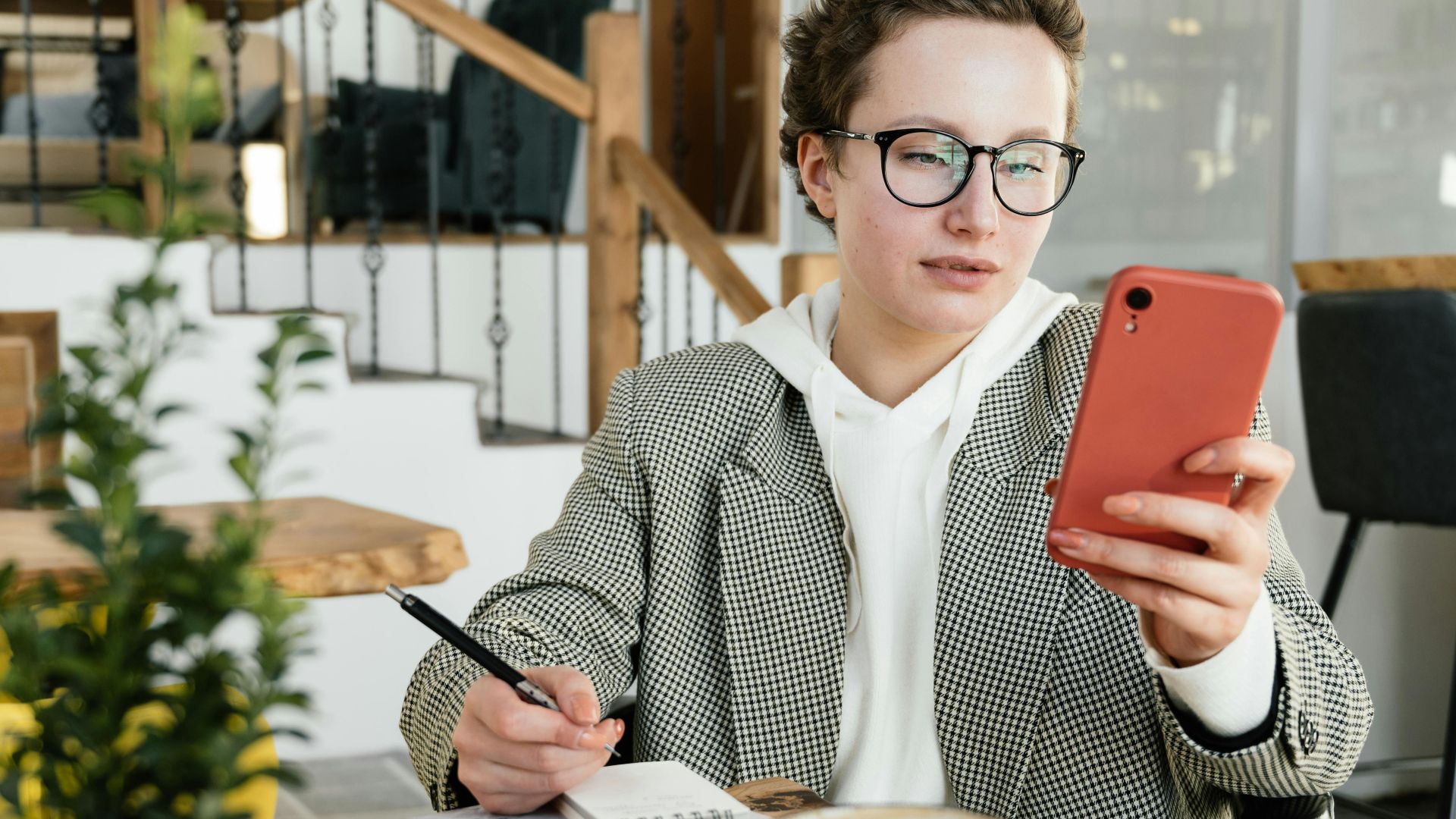 Adult woman in a café using a mobile phone and notebook, focused and engaged.
