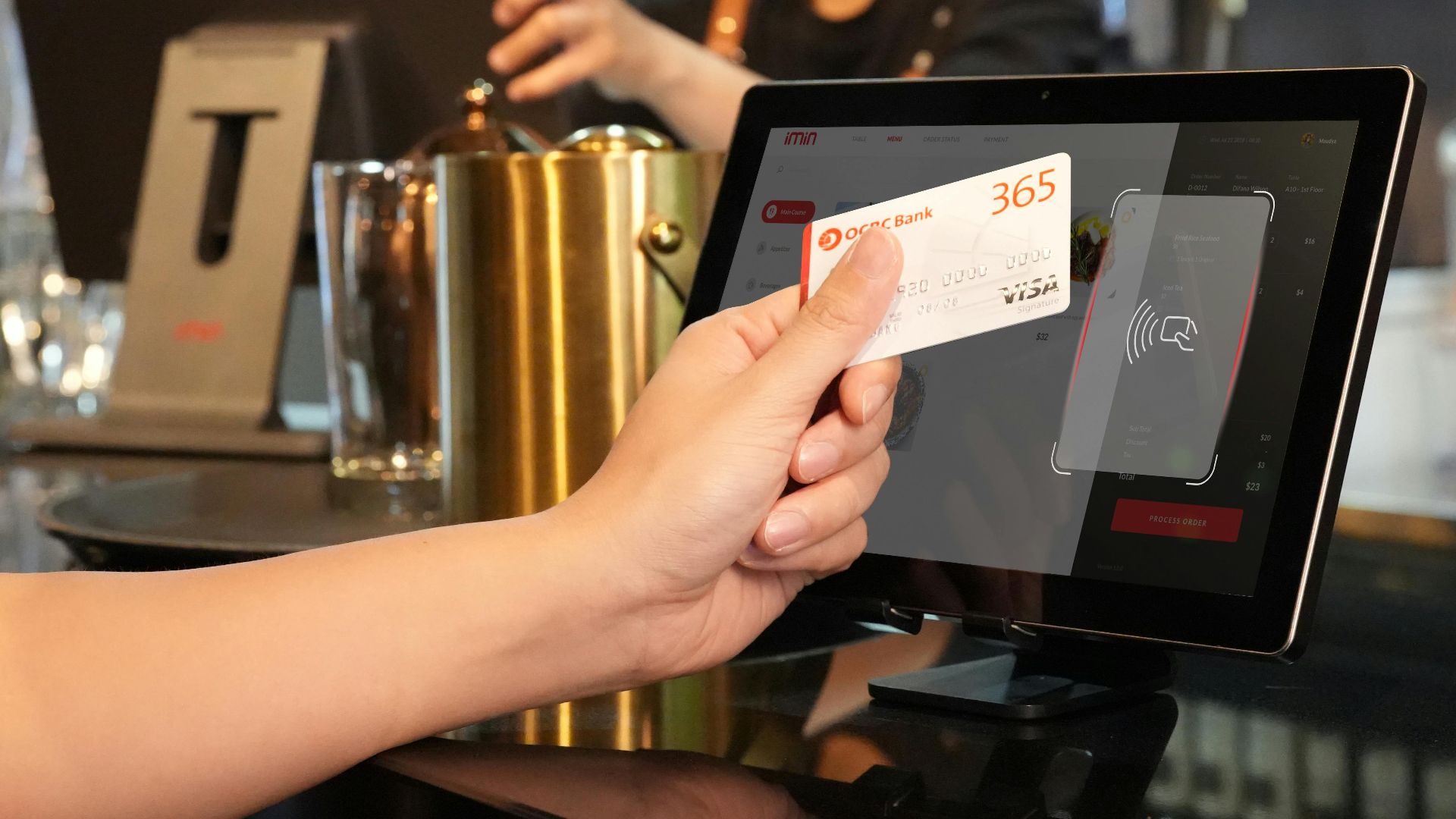 Person using contactless credit card payment at a modern bar, assisted by a cashier.