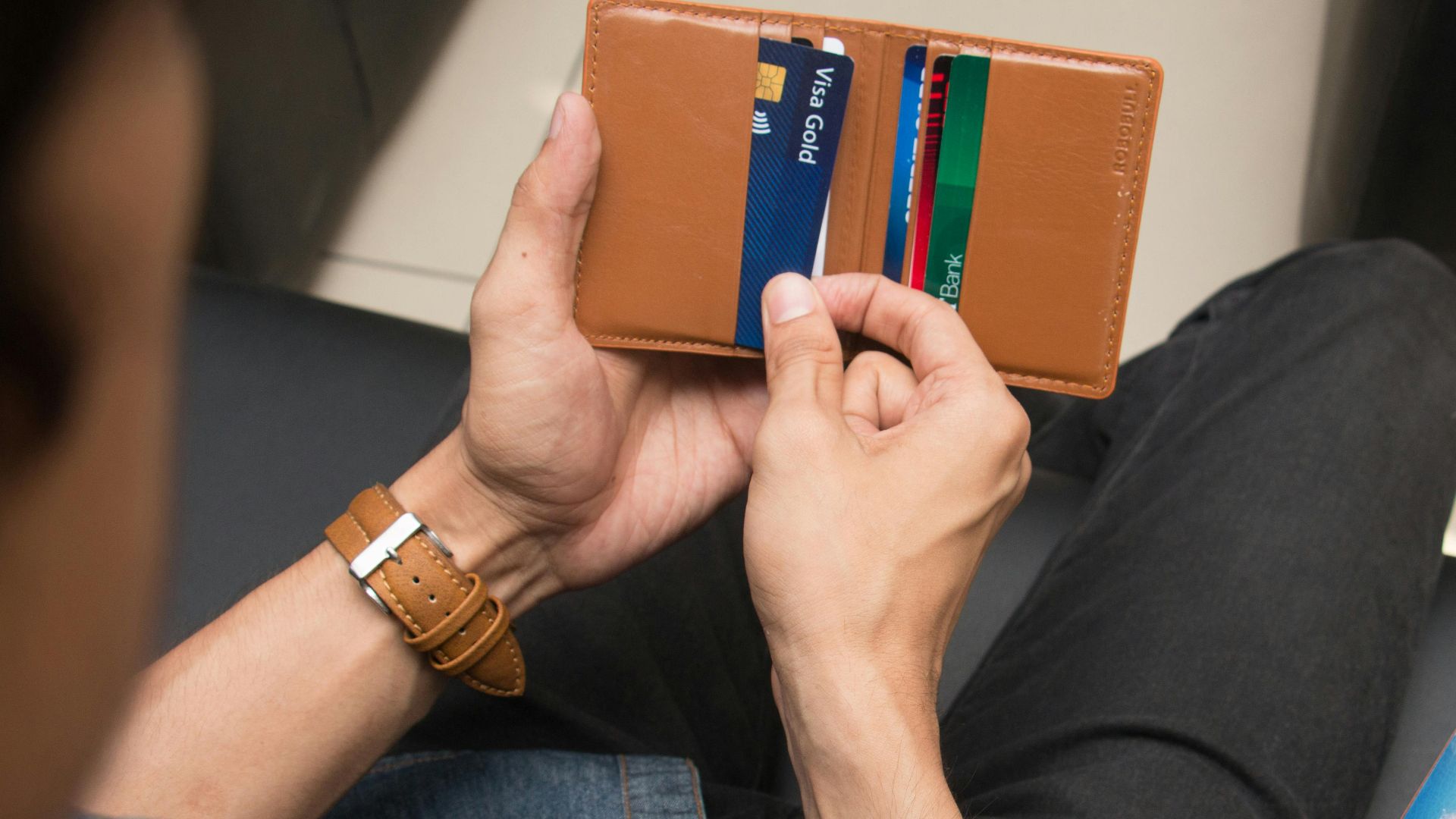 A close-up of a man holding a wallet containing credit cards and an ID inside a room.