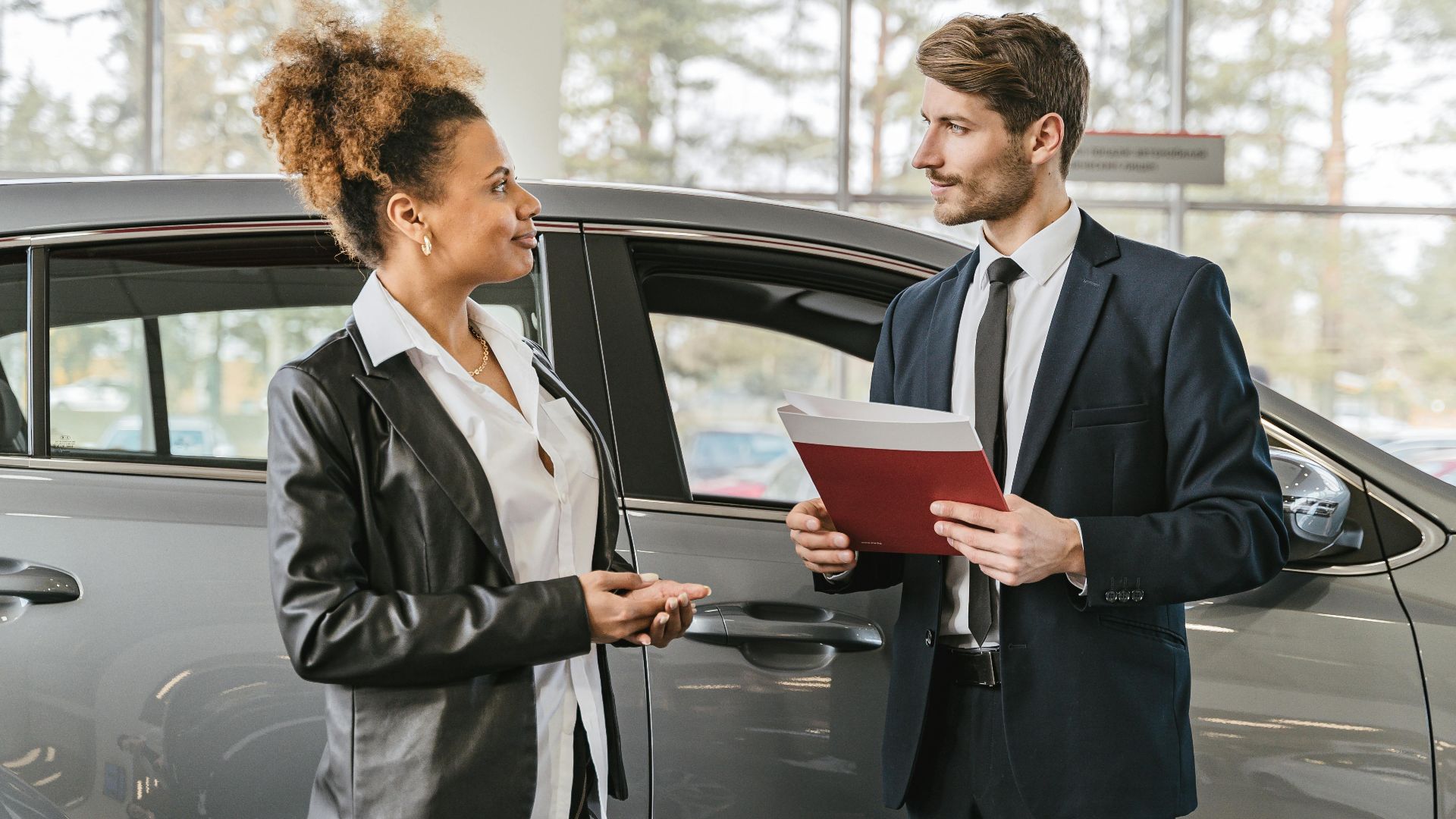 A woman discussing car purchase with a dealer inside a car dealership showroom.