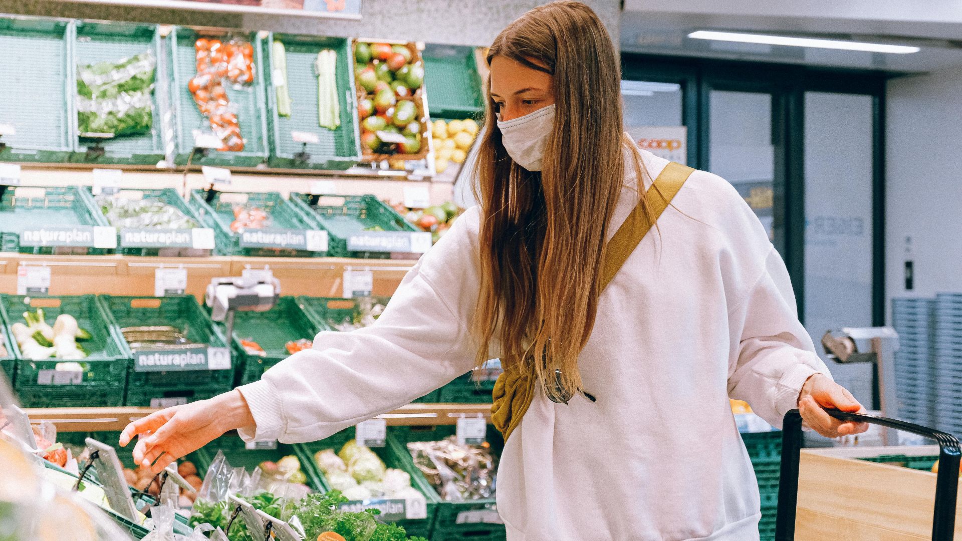 Woman wearing a face mask shopping for vegetables in a grocery store during the pandemic.