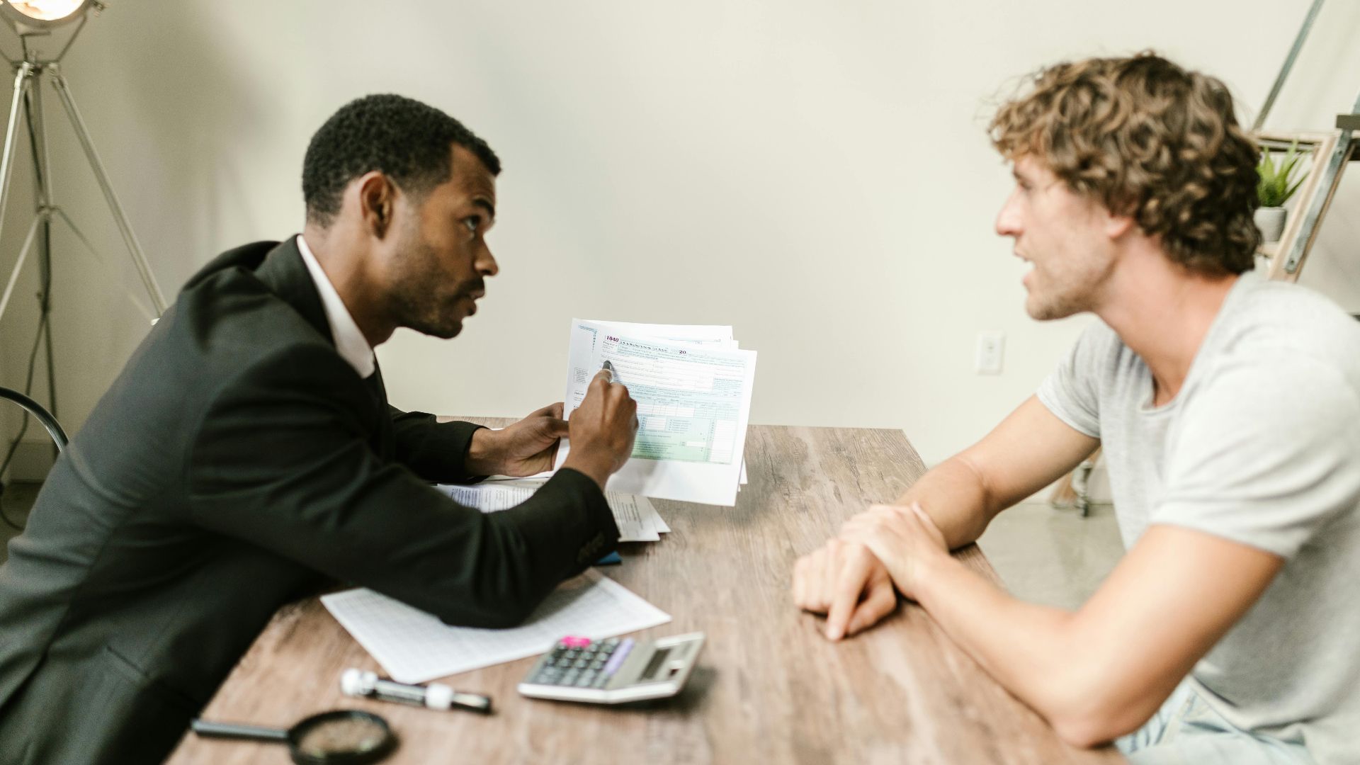 A financial advisor discusses paperwork with a client at a desk in a modern office.