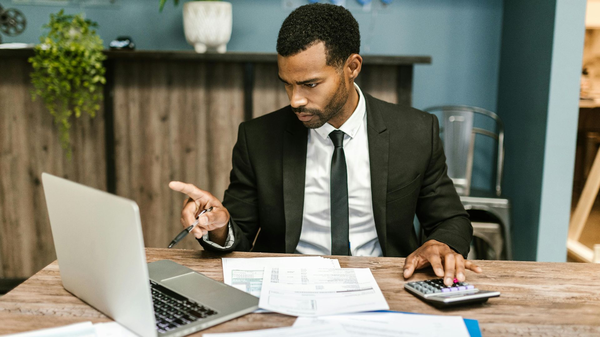 Professional man in a suit using a laptop and calculator in an office setting.