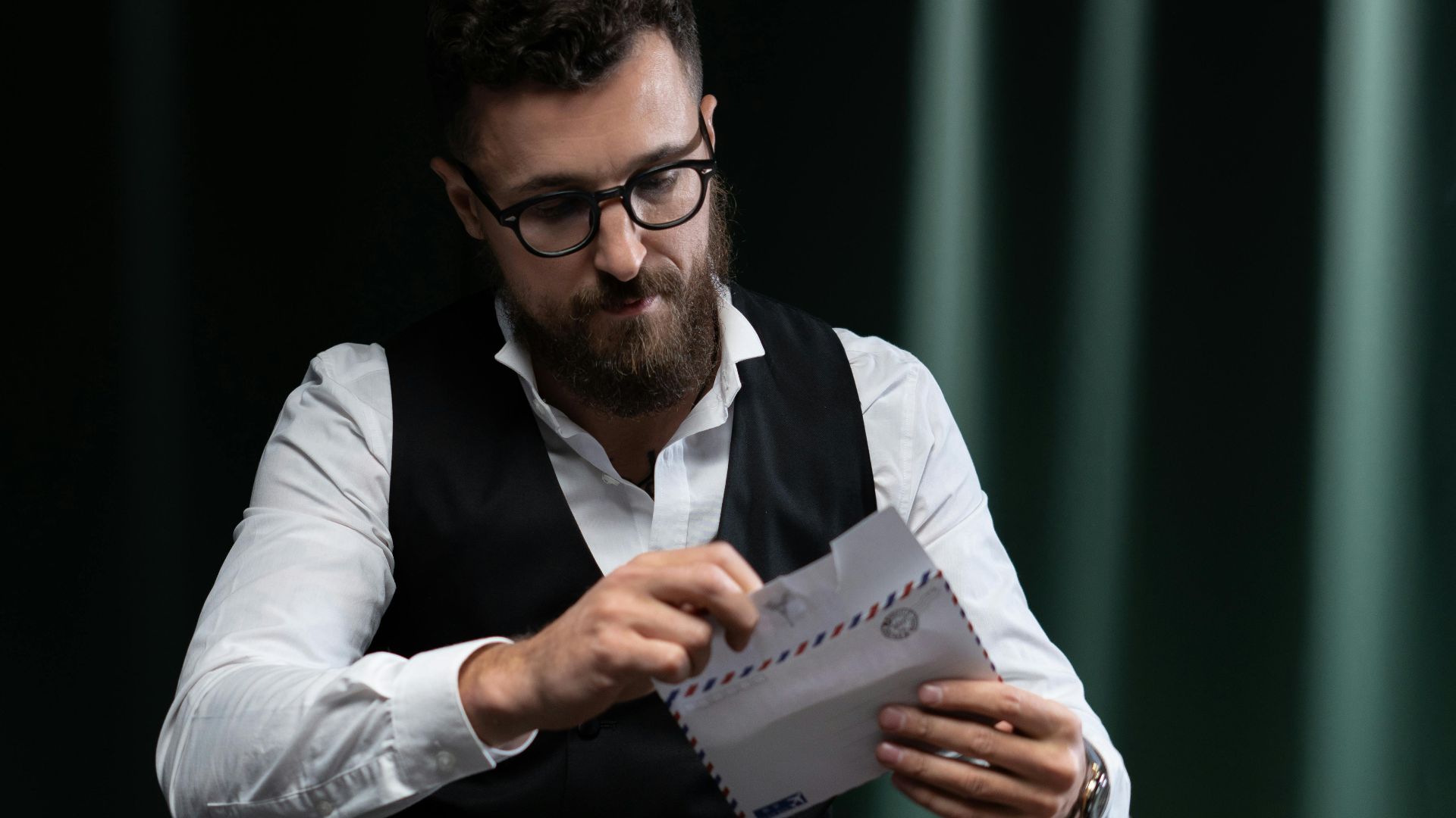 Bearded man at poker table reading a letter, surrounded by chips and gambling items.