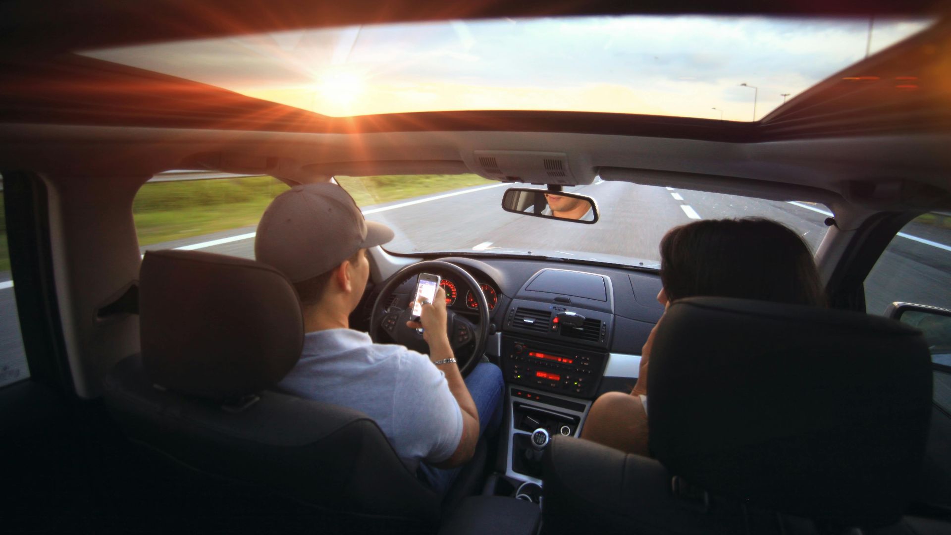 Driver using phone while driving at sunset with passenger in vehicle.