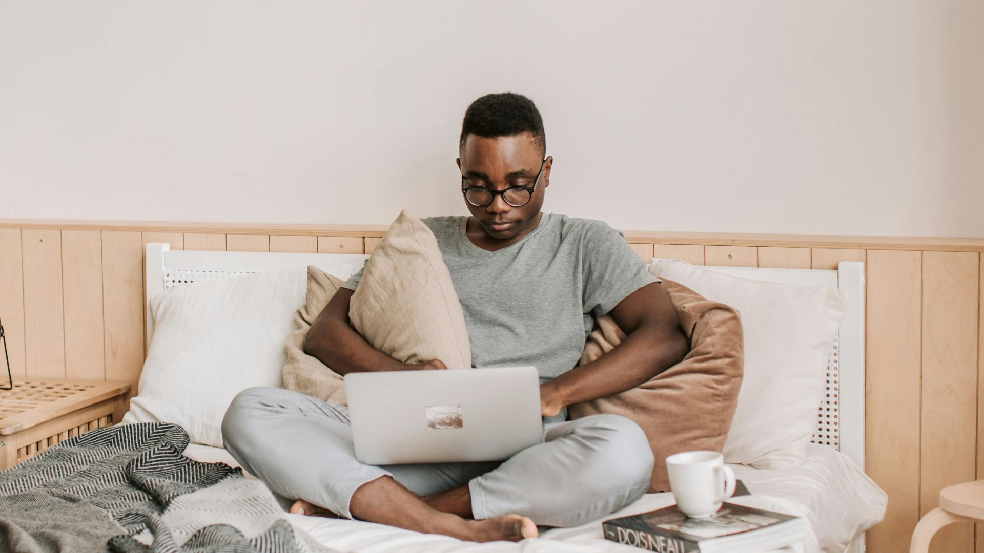 Adult man working from bed with laptop, relaxing in comfortable home setting.