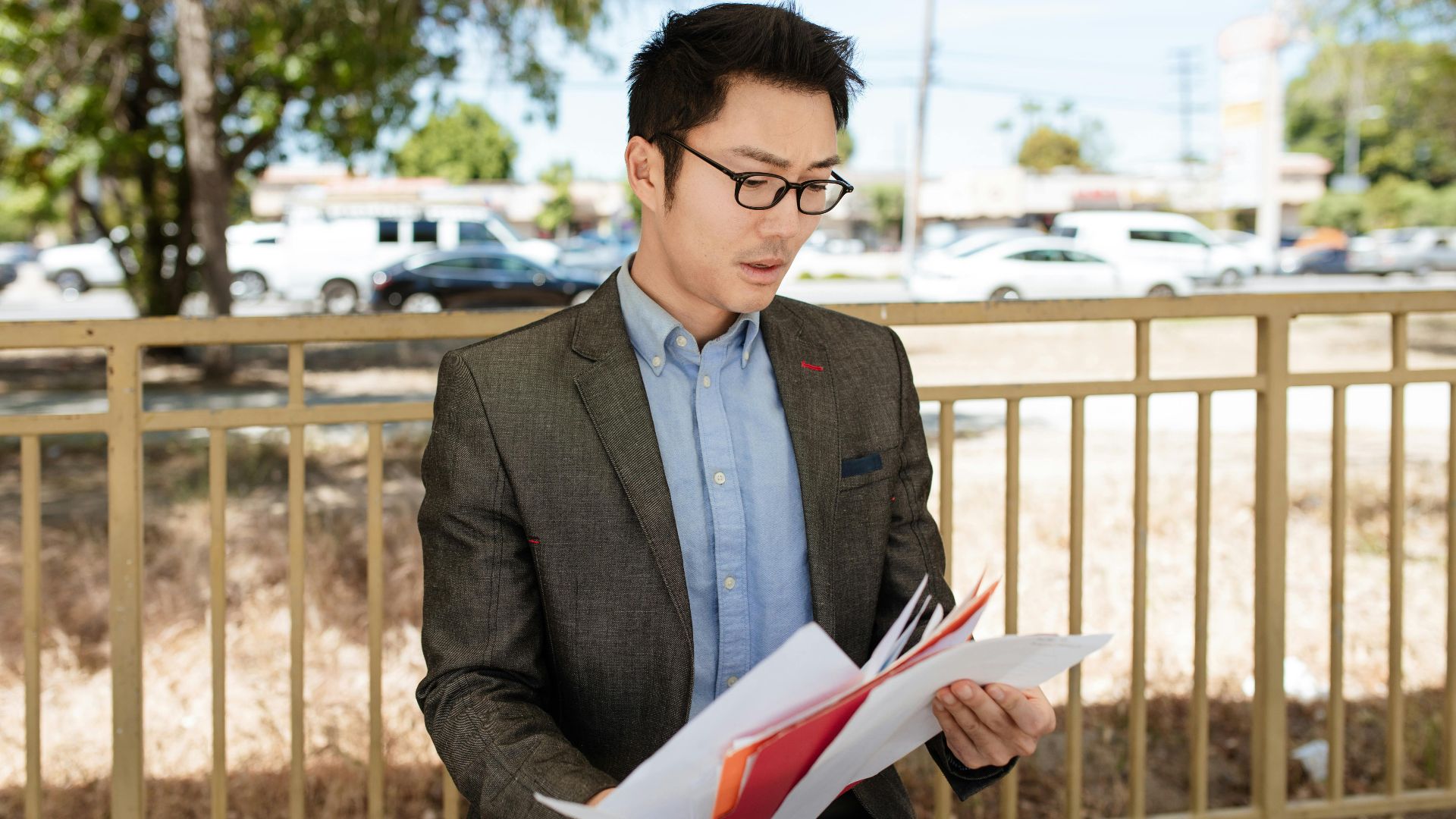 Asian businessman in a suit checking documents outdoors on a sunny day.