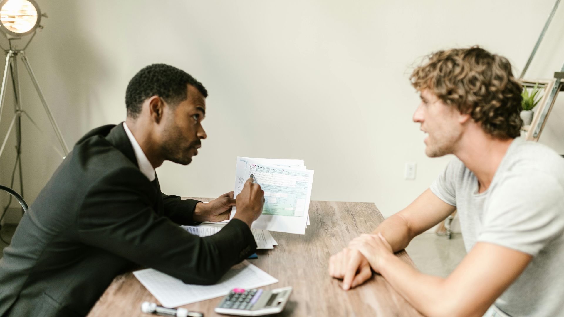 A financial advisor discusses paperwork with a client at a desk in a modern office.