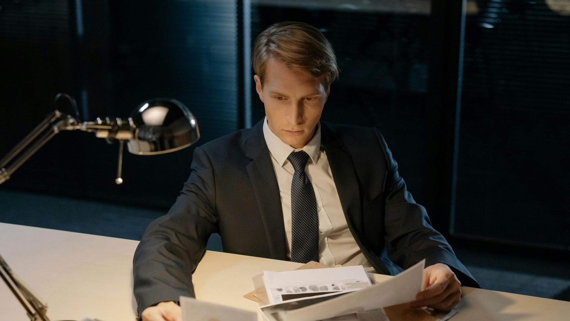 Focused investigator reviewing evidence in a dimly lit office setting.