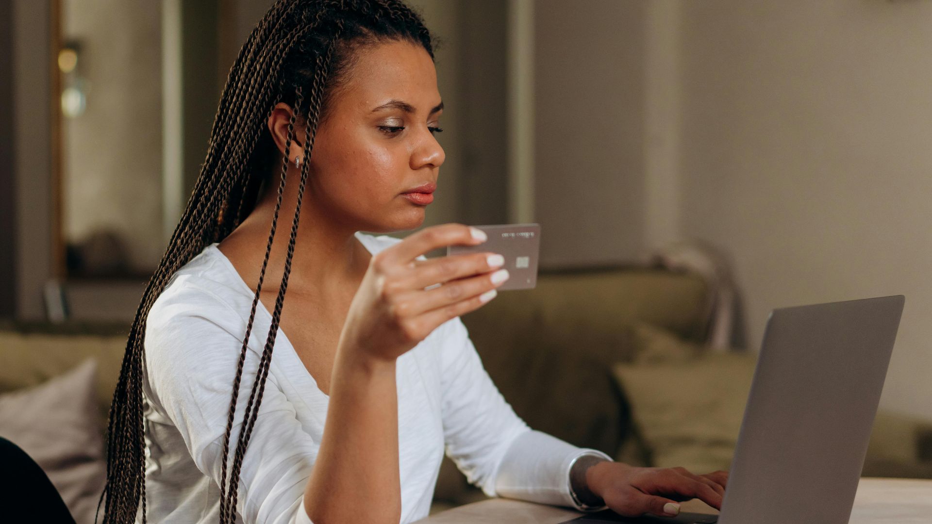 A woman with braided hair makes an online transaction using a credit card and laptop at home.