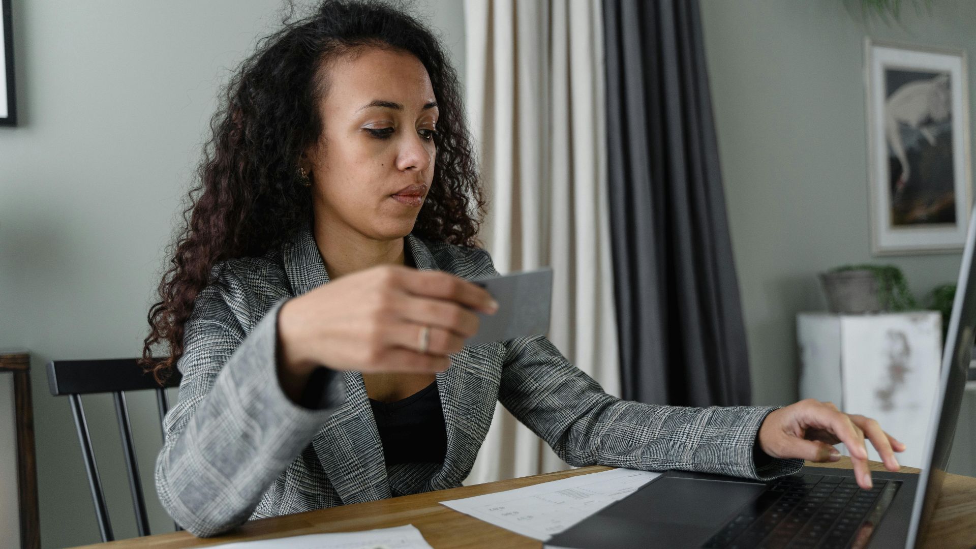 Woman using a laptop and managing finances with cash and card on a wooden table indoors.