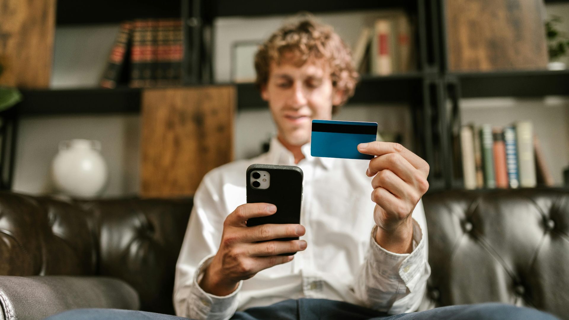 A man smiles while using his smartphone and credit card for online shopping.