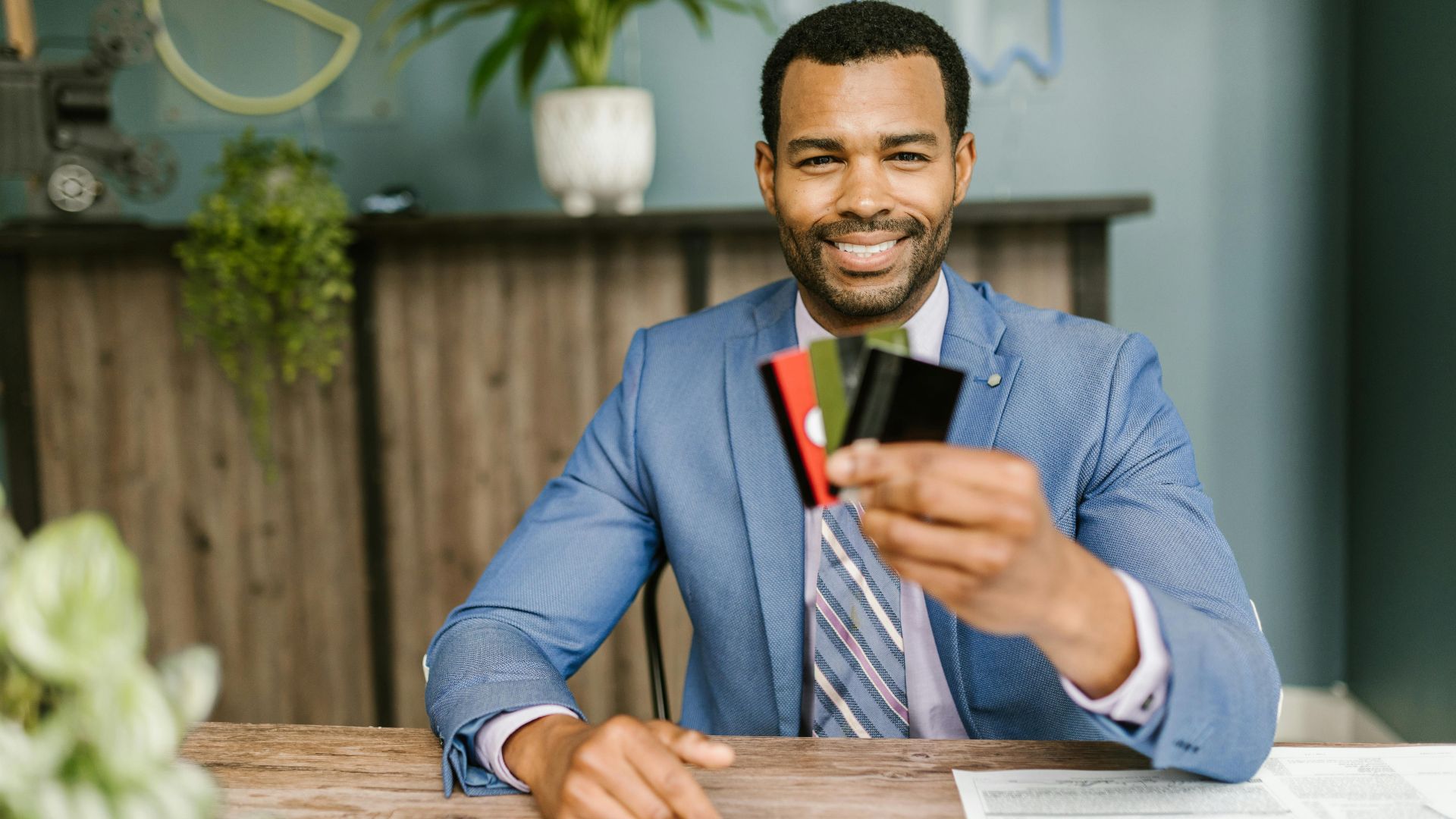 Smiling African American man in a suit holding credit cards at a business desk.