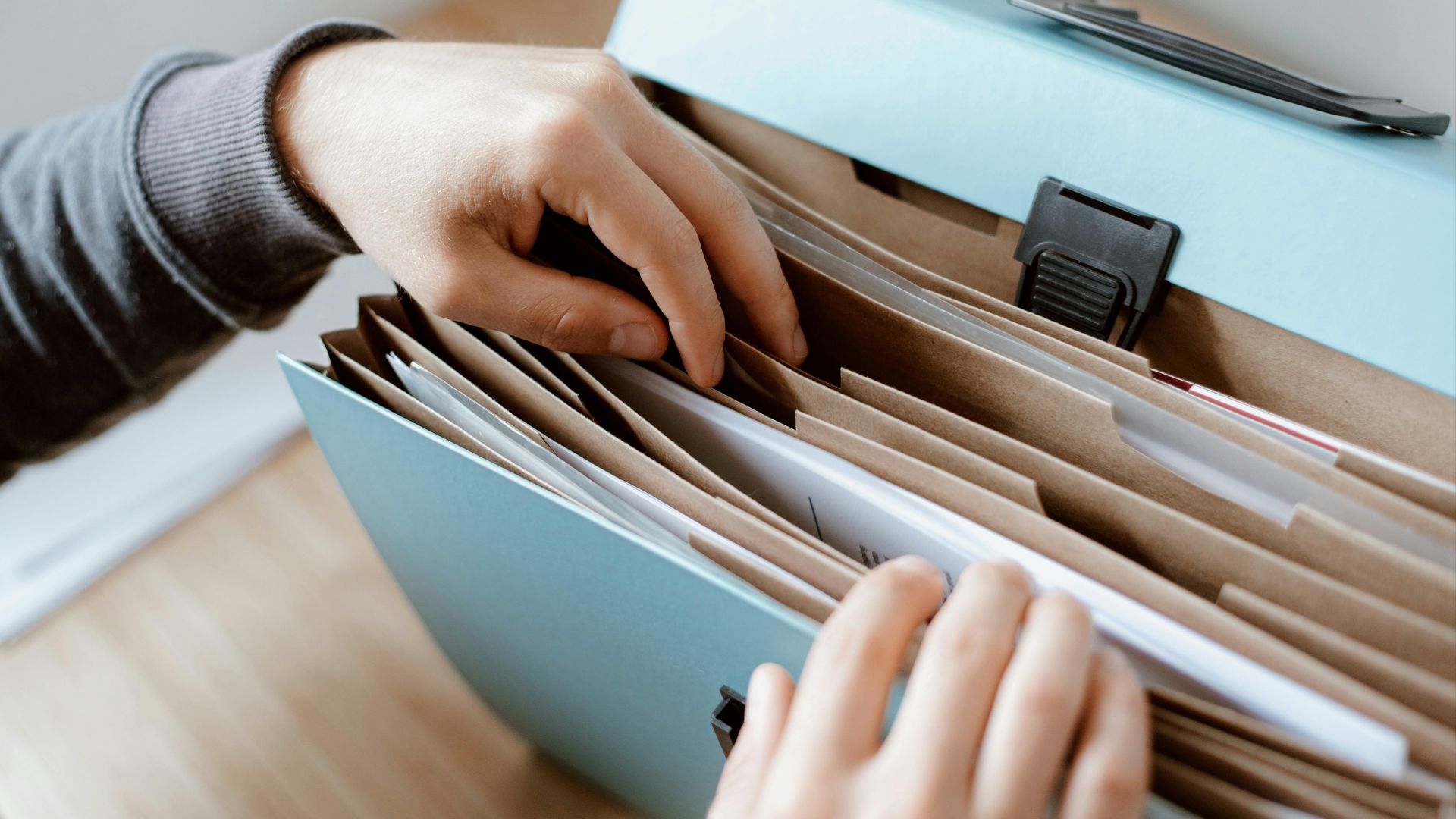 Close-up of hands organizing papers in a blue folder, ideal for business and office concepts.