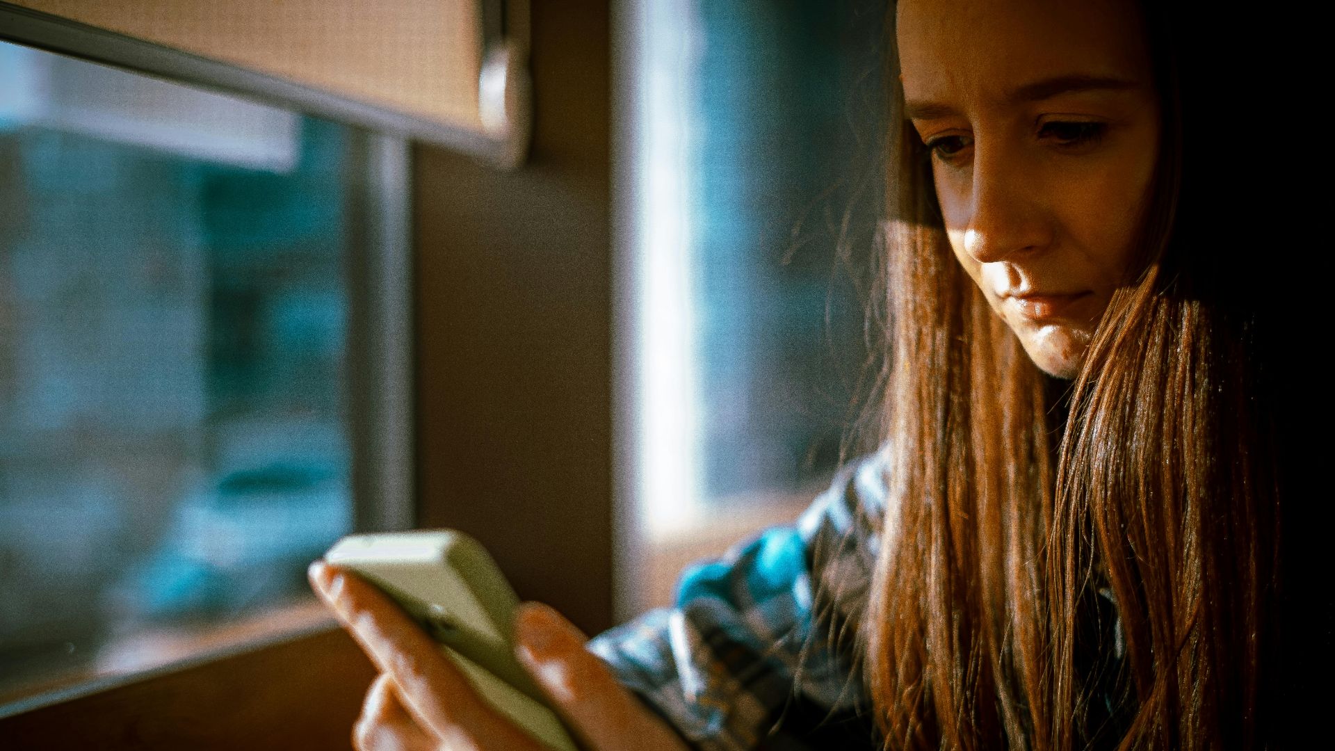 Young woman looking at smartphone with sunlight streaming in through a window.
