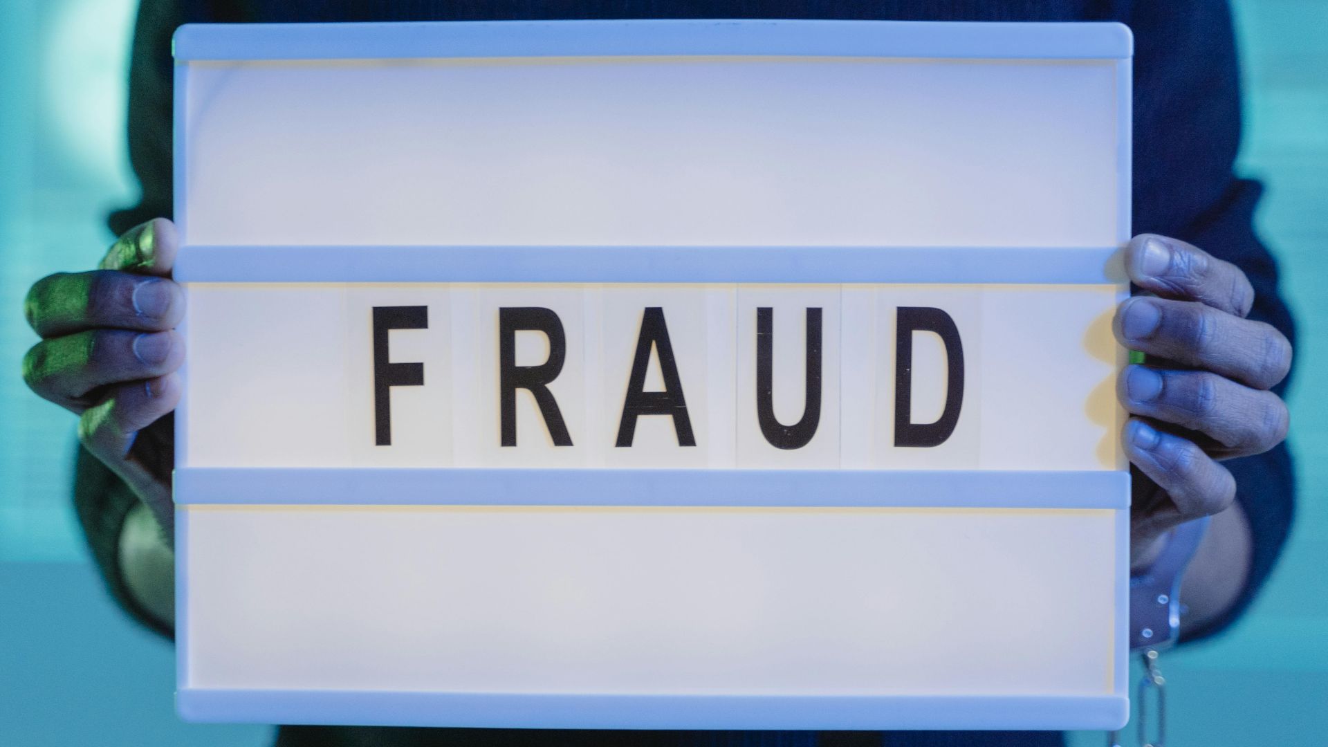 Close-up of hands holding a sign with 'fraud', illuminated in blue light.