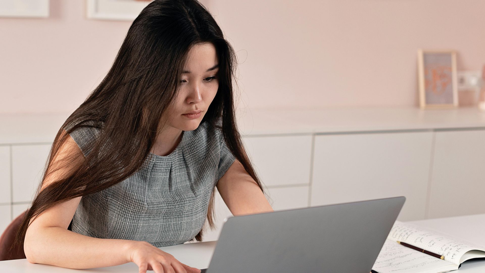 Asian woman in a modern office setting working on a laptop, symbolizing entrepreneurship and professionalism.