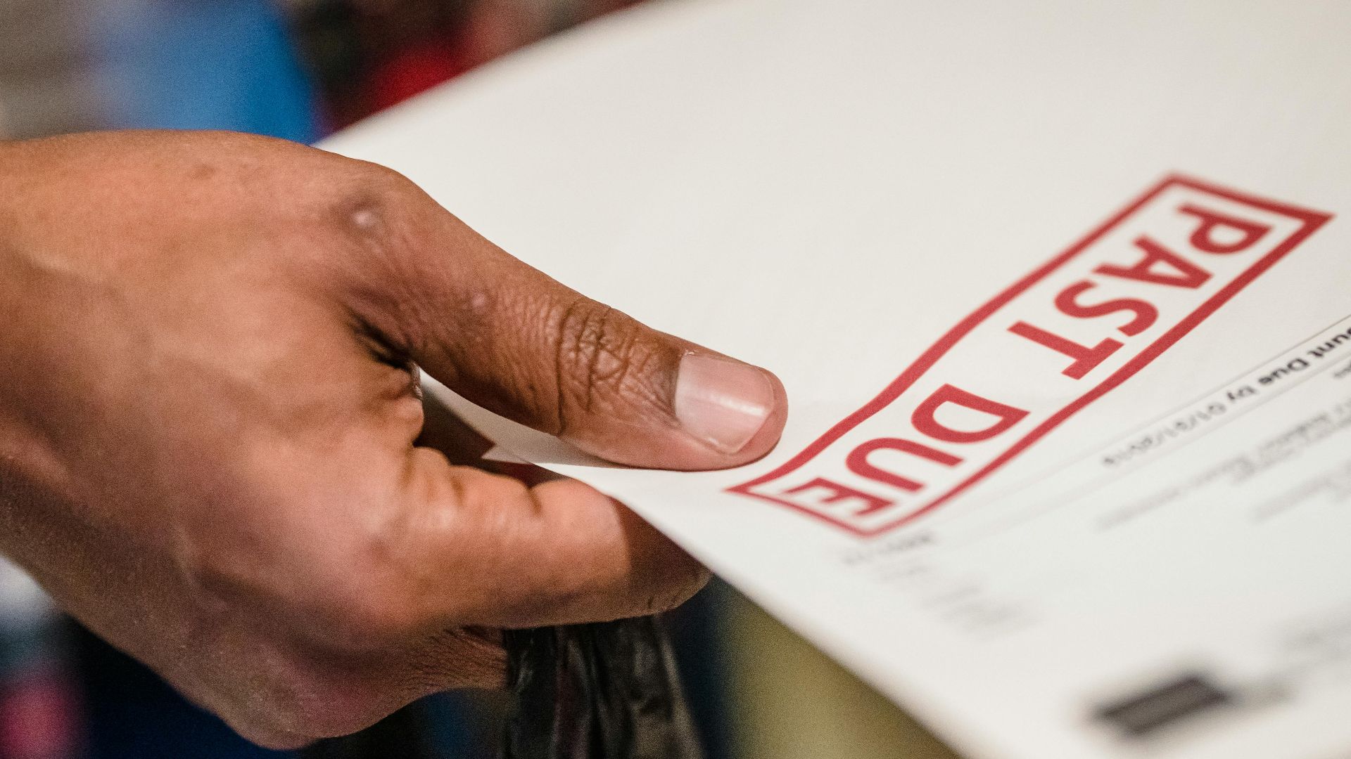 A close-up of a hand holding a document with a 'Past Due' stamp, highlighting financial urgency.