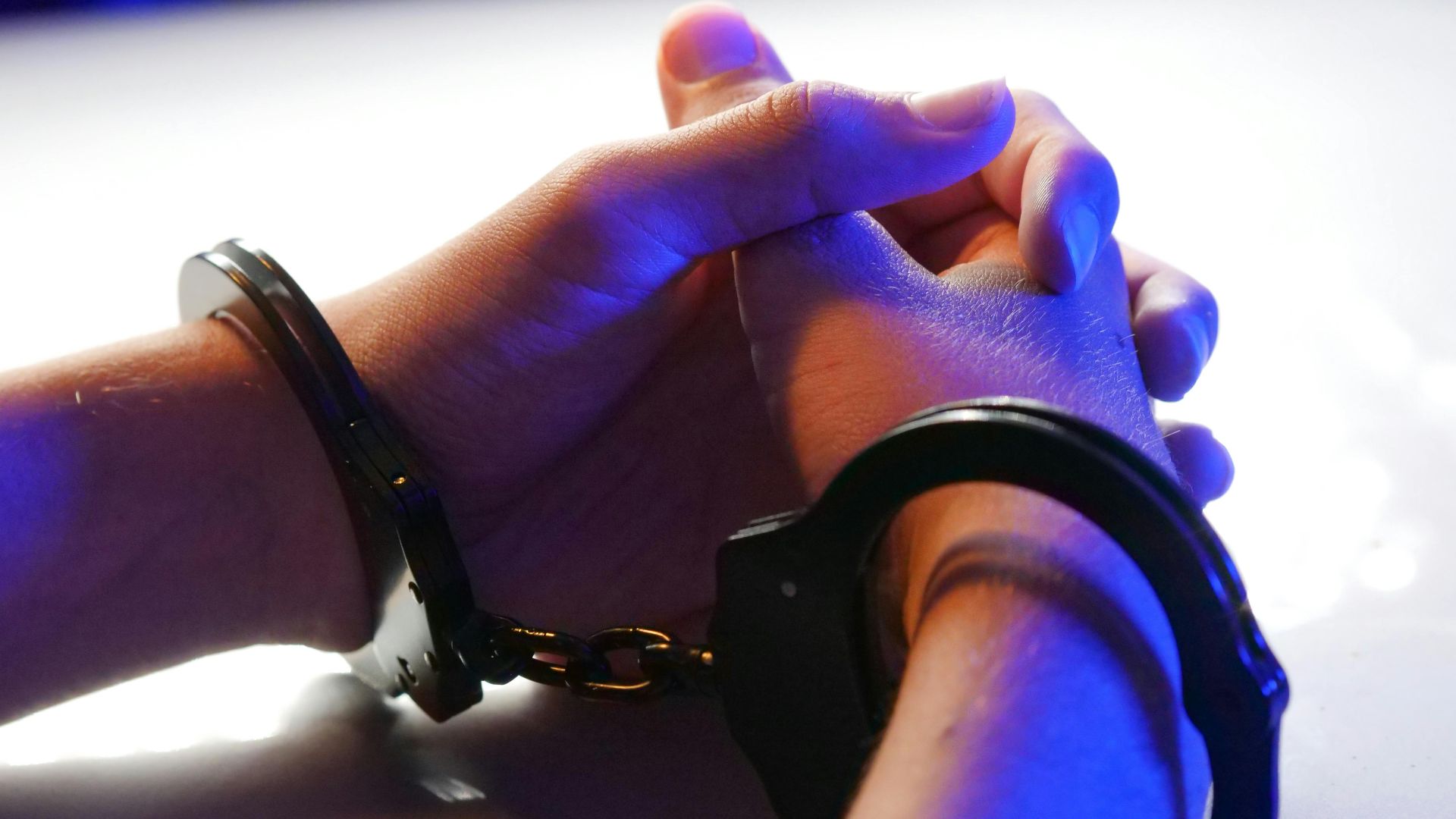 Close-up of handcuffed hands under blue police light, signifying arrest or detention.