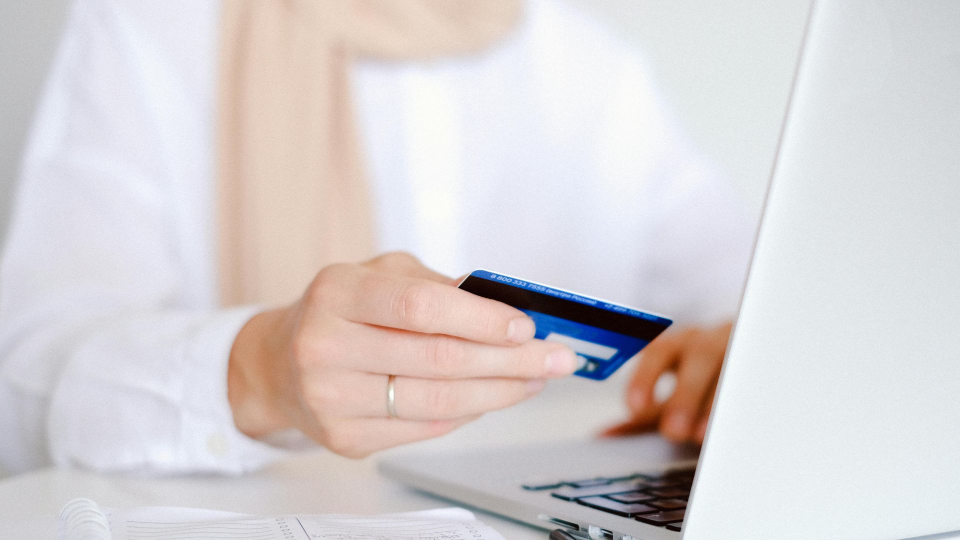 Close-up of a person holding a credit card while using a laptop for online shopping.