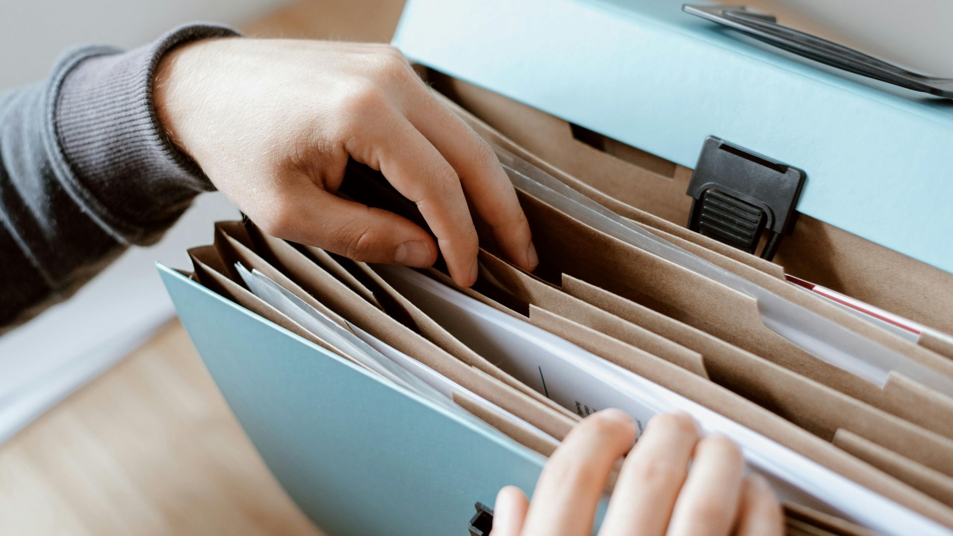 Close-up of hands organizing papers in a blue folder, ideal for business and office concepts.