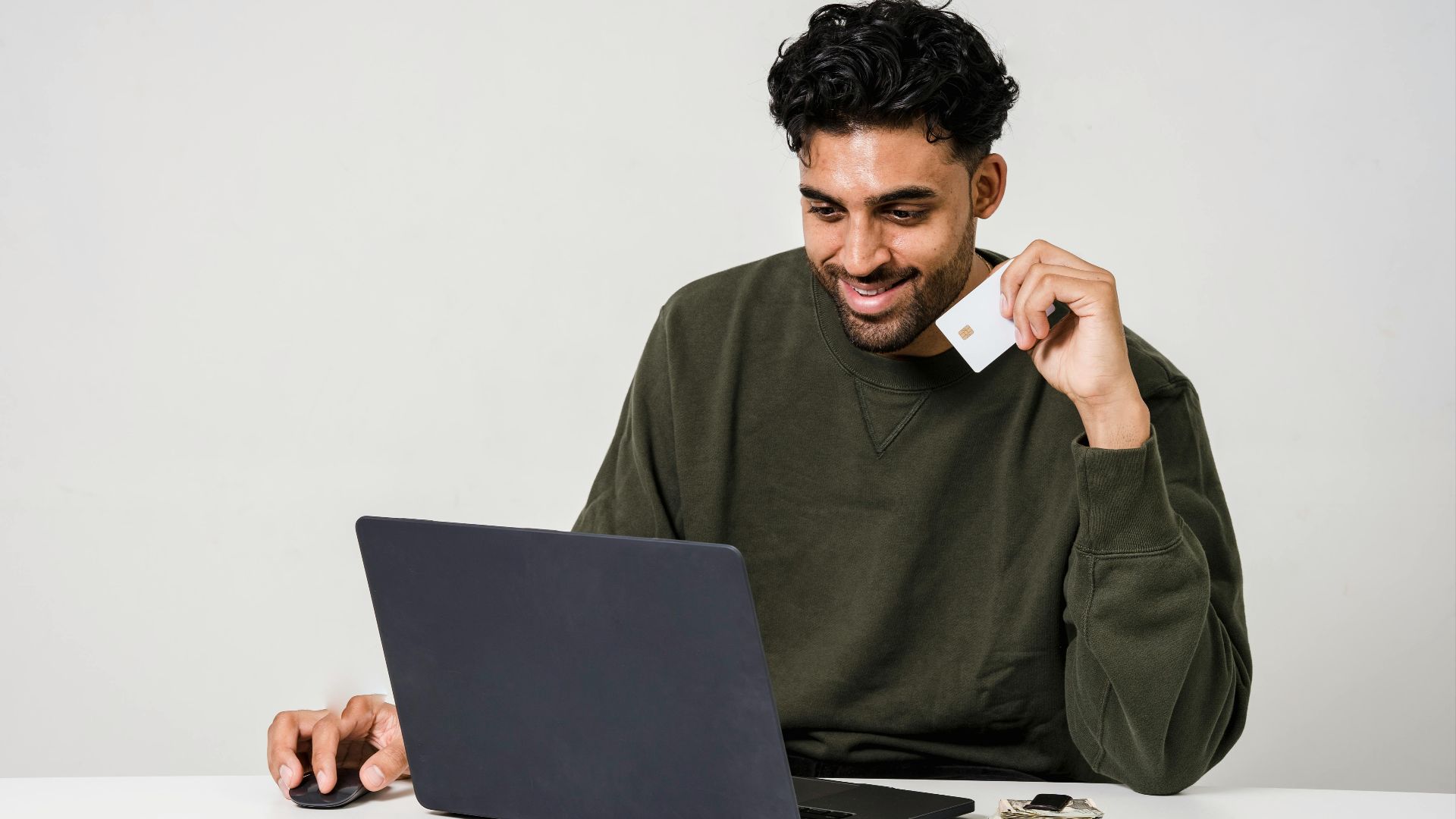 A man smiling while using a laptop and holding a credit card for online shopping.