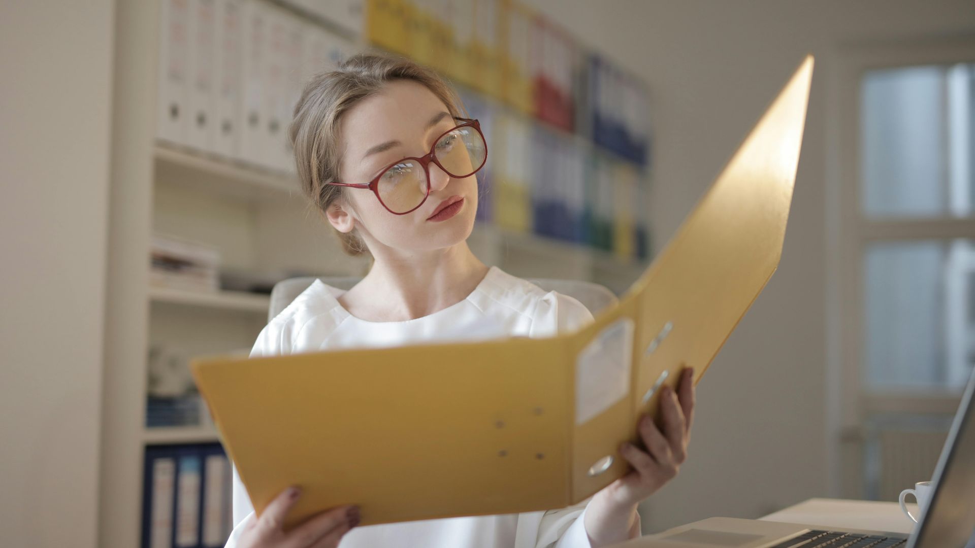 Caucasian woman intensely reading documents in an office setting.