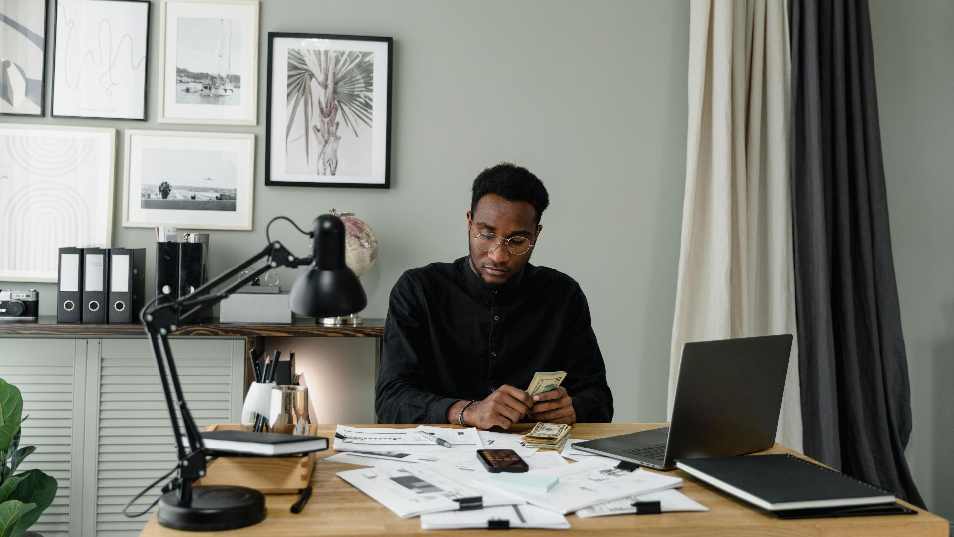 Serious businessman counting money at a desk in a modern office setting.