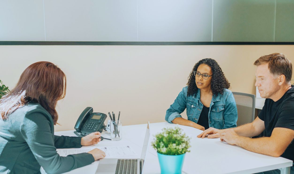Unrecognizable worker talking to multiethnic clients at desk with laptop