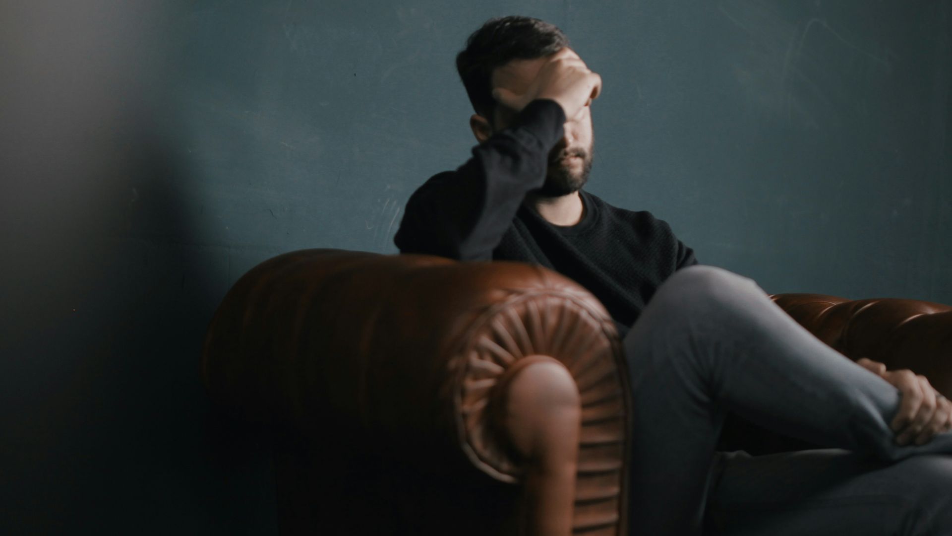 a man holds his head while sitting on a sofa