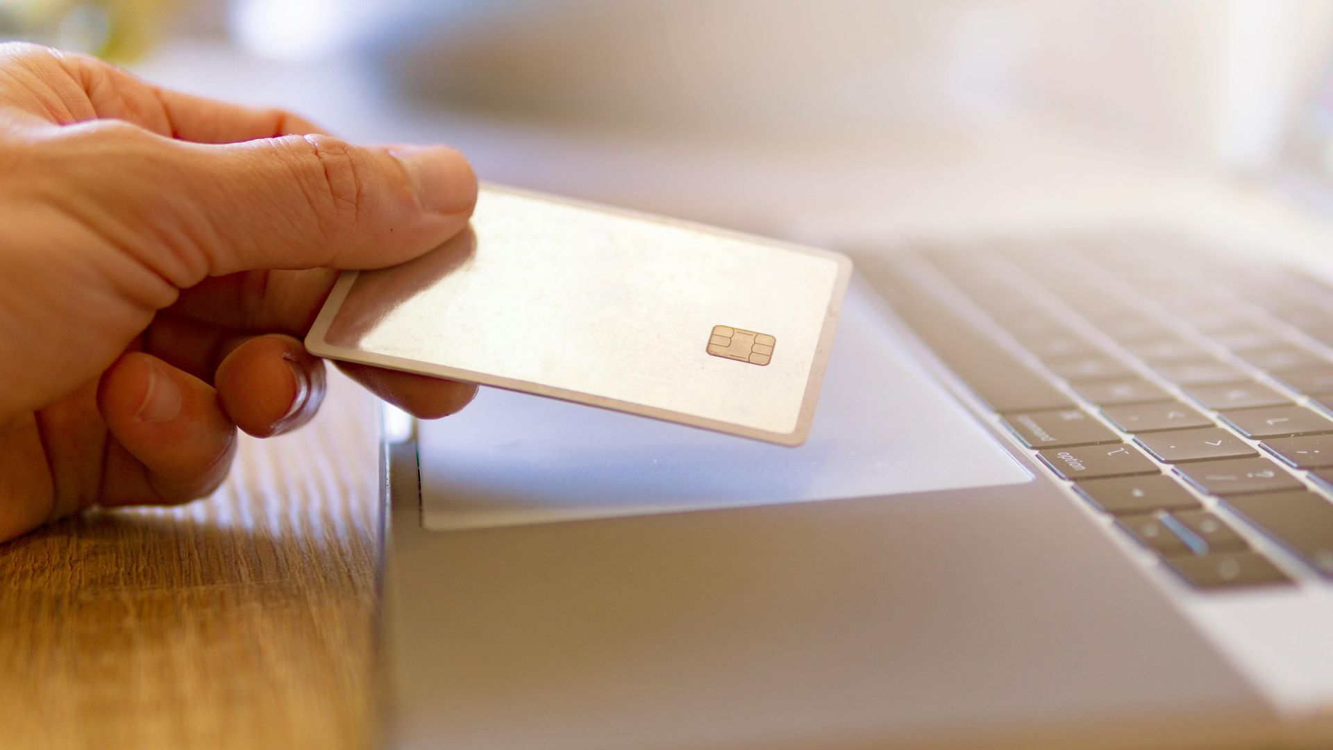 A person holds a credit card near a laptop for online shopping.