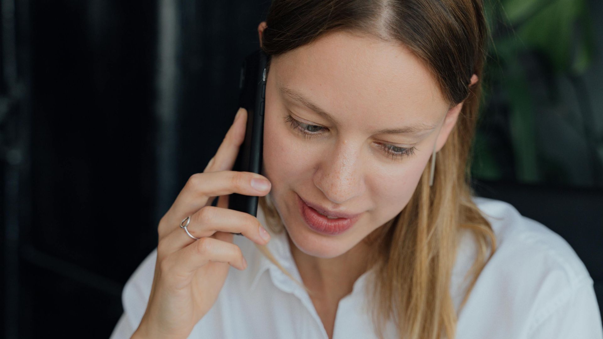 A professional woman in a white shirt making a phone call in an indoor setting, showing communication and business engagement.