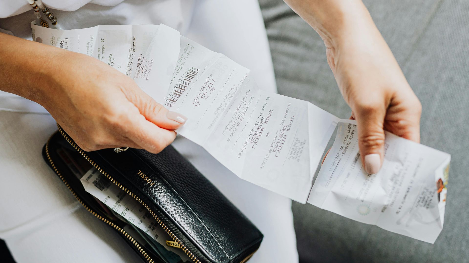 Close-up of a woman's hands managing multiple receipts taken from a black wallet.