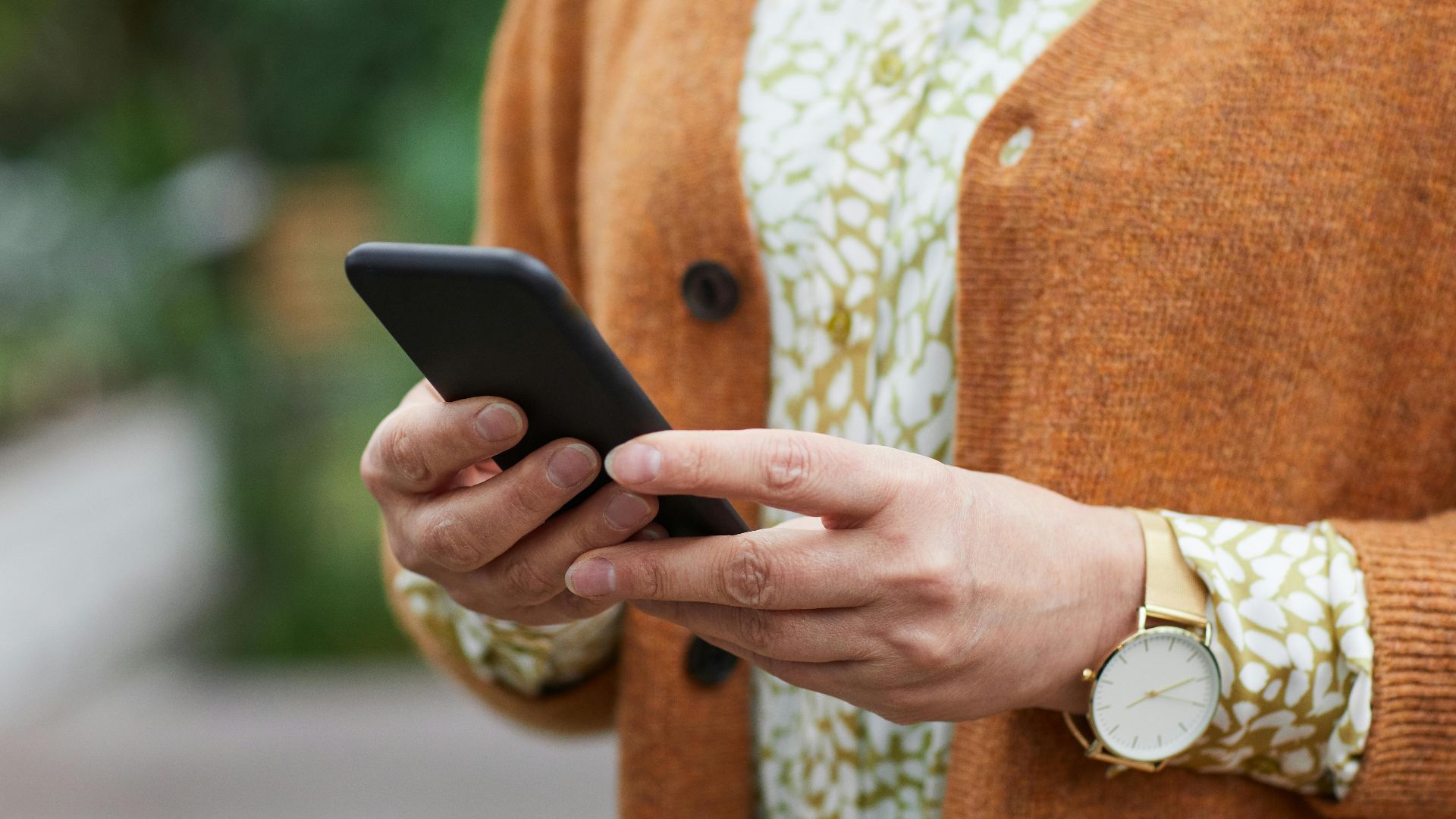 Elderly person's hands holding a smartphone in a casual setting, wearing a watch.