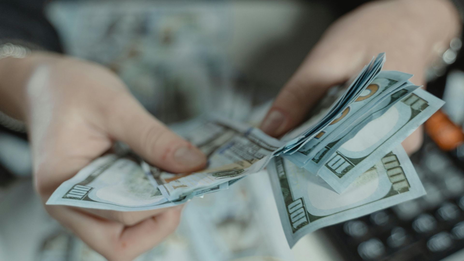 Close-up of hands counting hundred dollar bills with a calculator in the background.