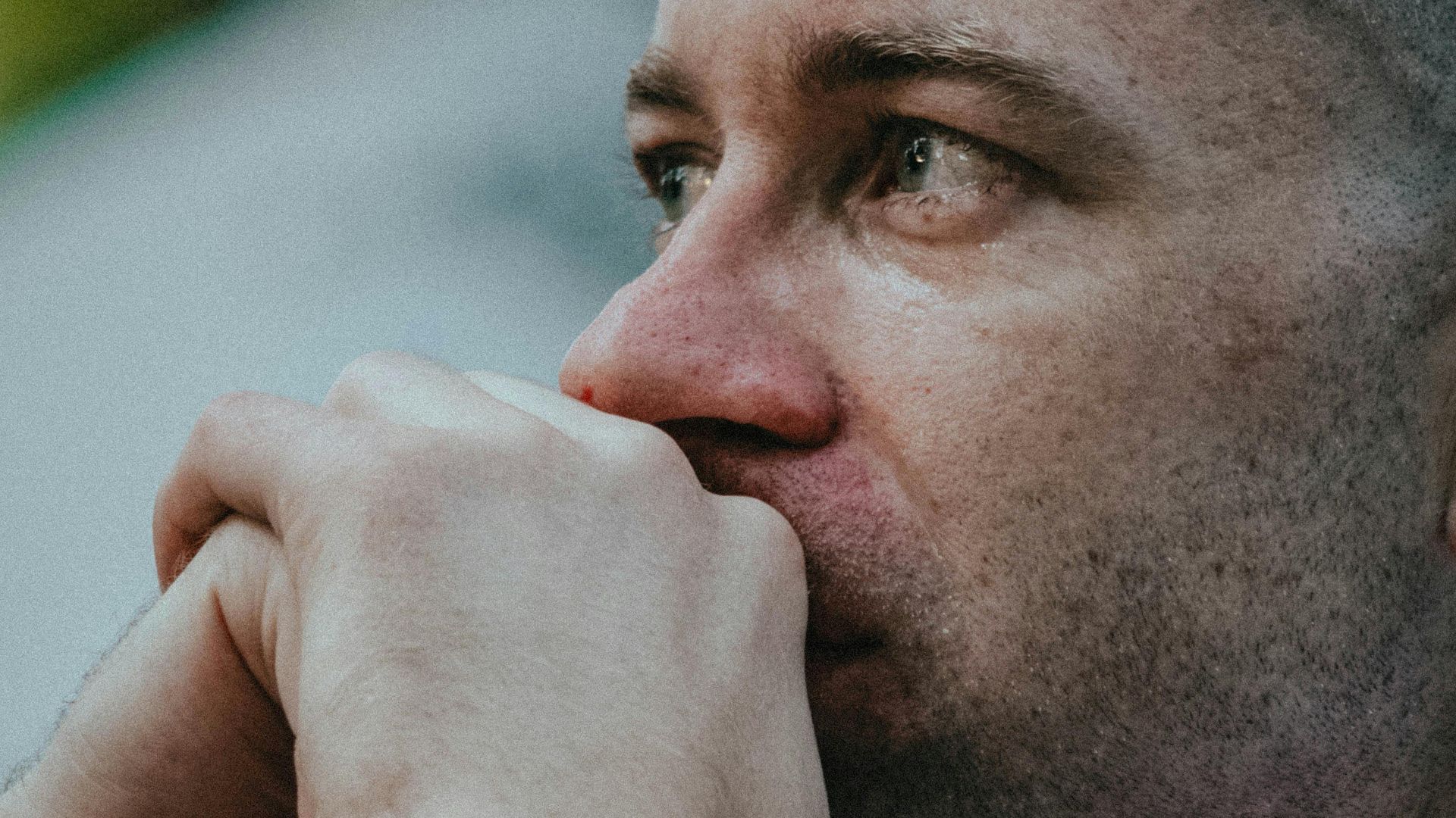 Side profile of a man deep in thought, hands clasped, outdoors.