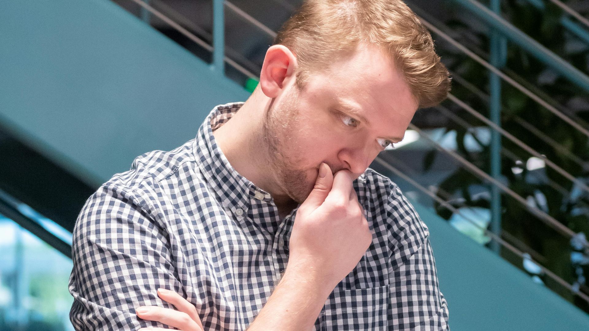 Man in a plaid shirt deep in thought while working in a modern office.