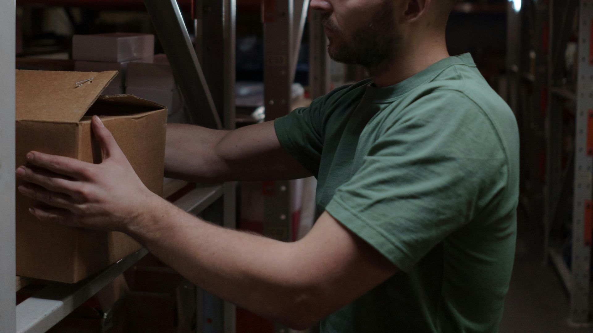 Warehouse worker organizing inventory with focus and efficiency in dim lighting.