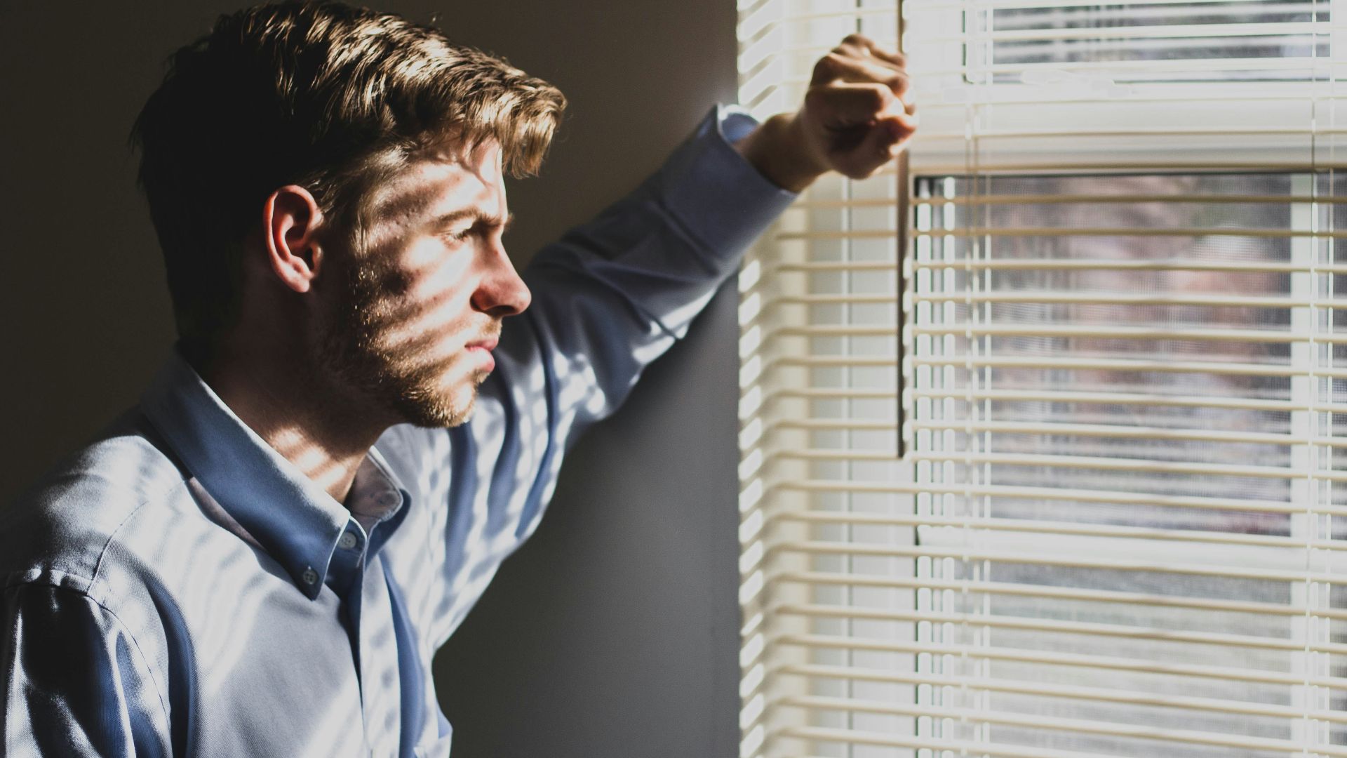 person near clear glass window pane and window blinds low-light photography
