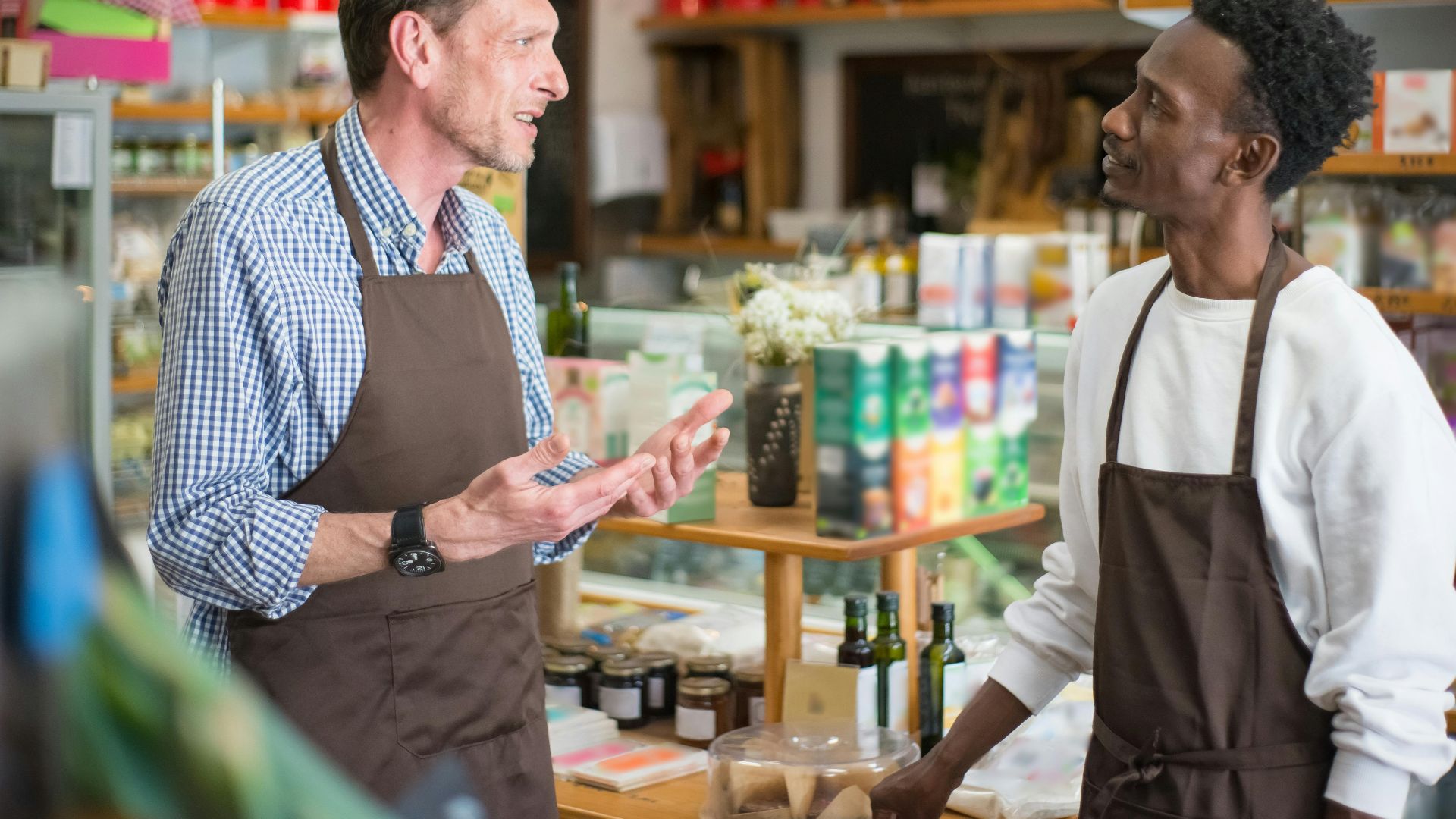 Two colleagues in aprons conversing in a grocery store setting.