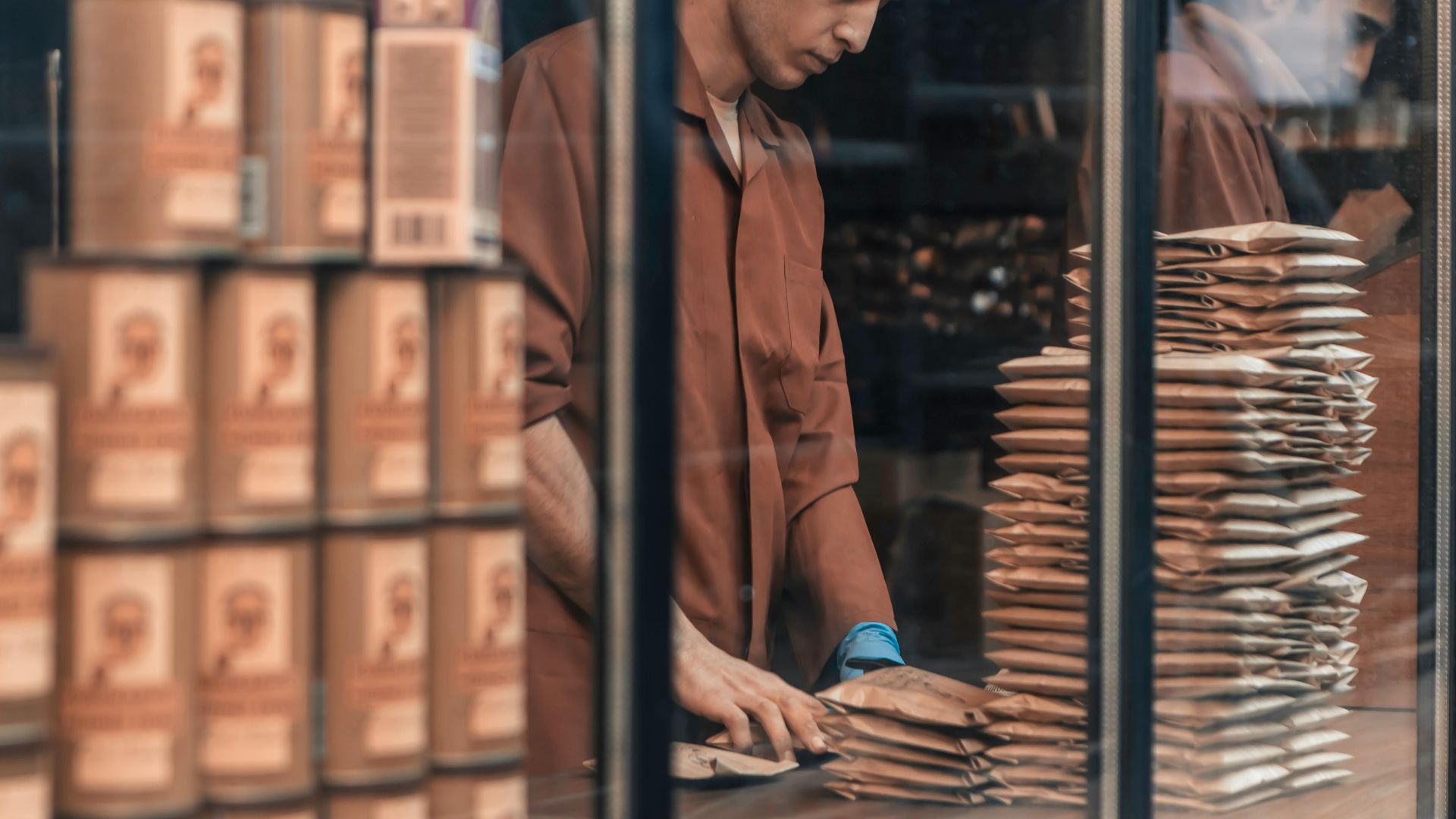 A man packing goods behind a glass window, showcasing a work environment with reflections and stacked items.