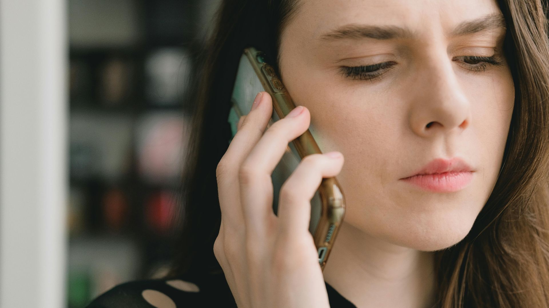 Close-up of a woman engaged in a phone conversation indoors, depicting a thoughtful expression.