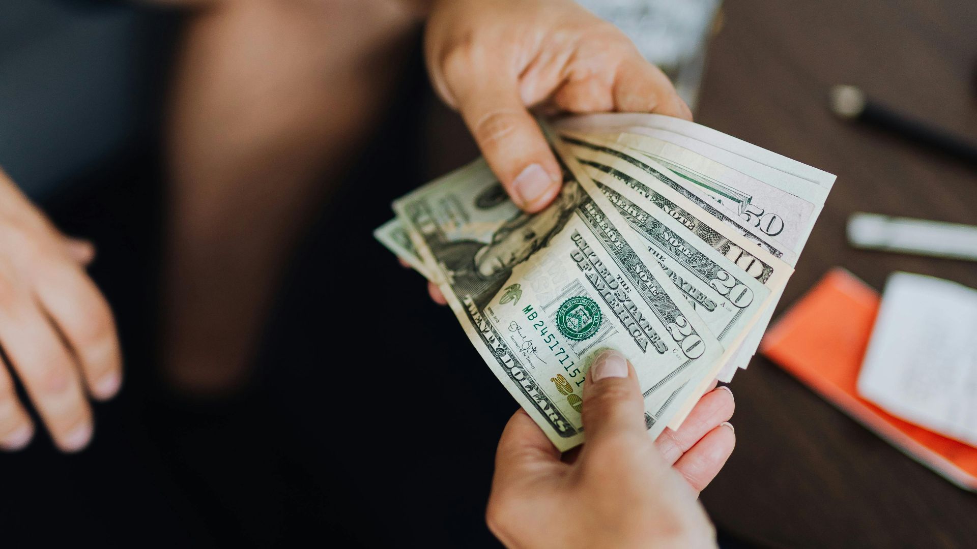 A close-up view of hands exchanging dollar bills indoors, symbolizing payment.