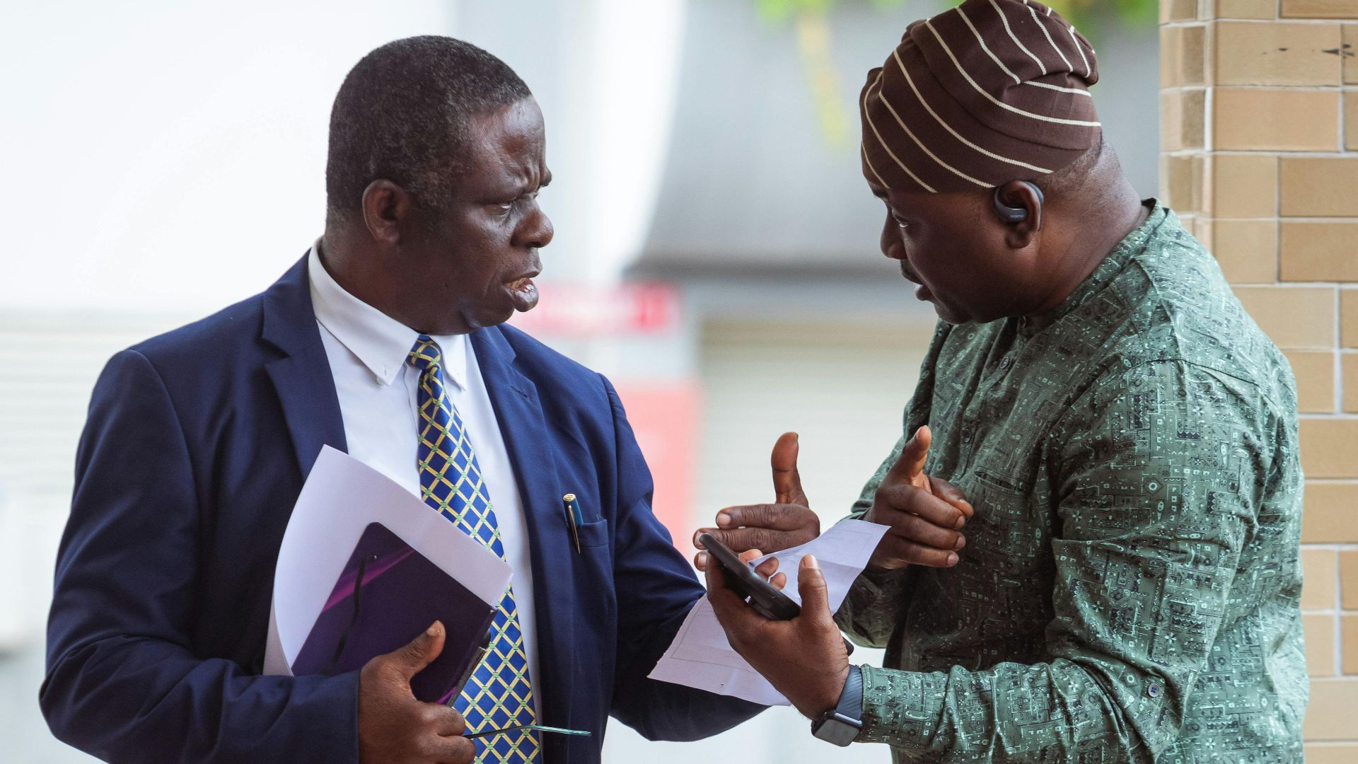 Two men engaged in a serious discussion outside, holding business documents.