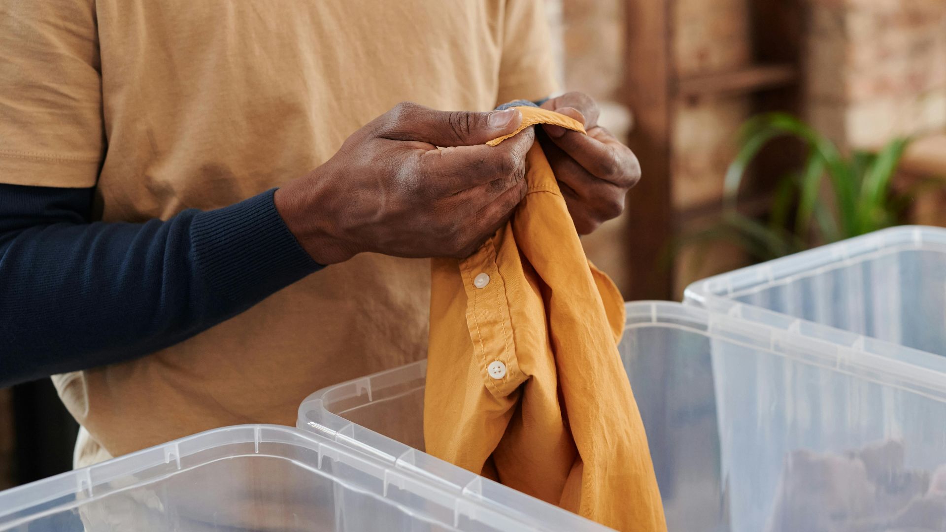 A volunteer sorting clothes into clear plastic bins indoors.