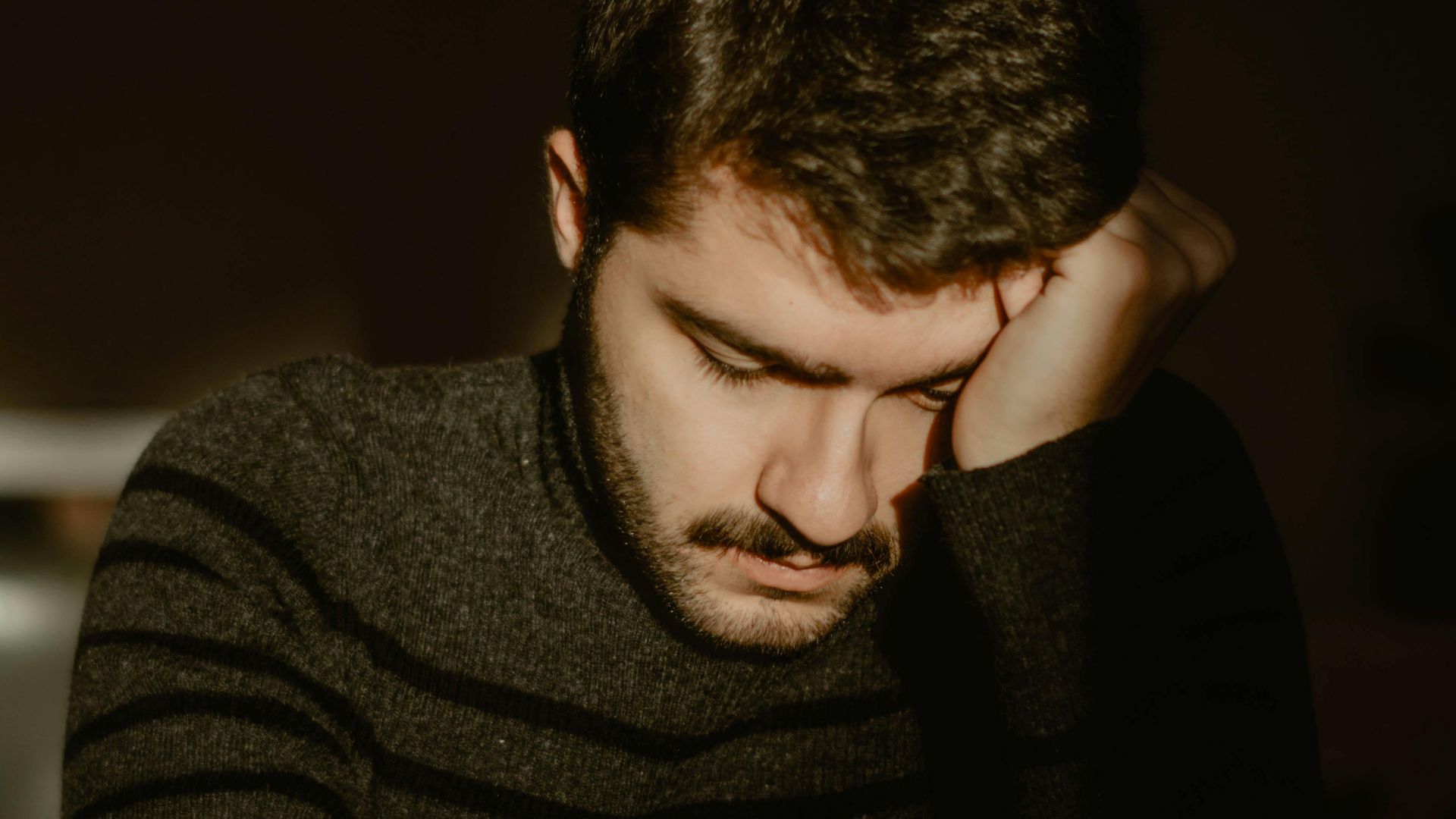 Portrait of a young man sitting alone indoors, reflecting in a dimly lit room.