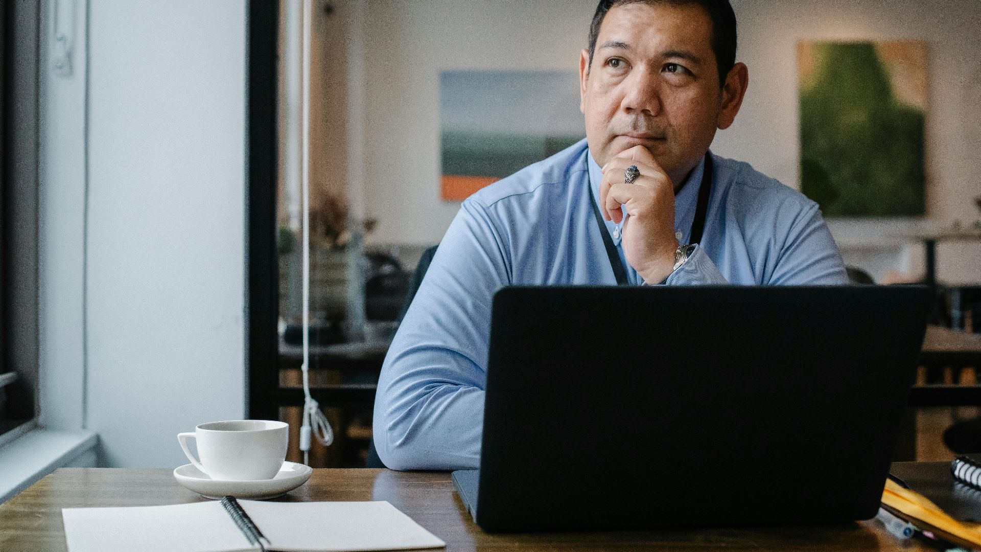 A businessman deep in thought while working on a laptop in a modern office setting.