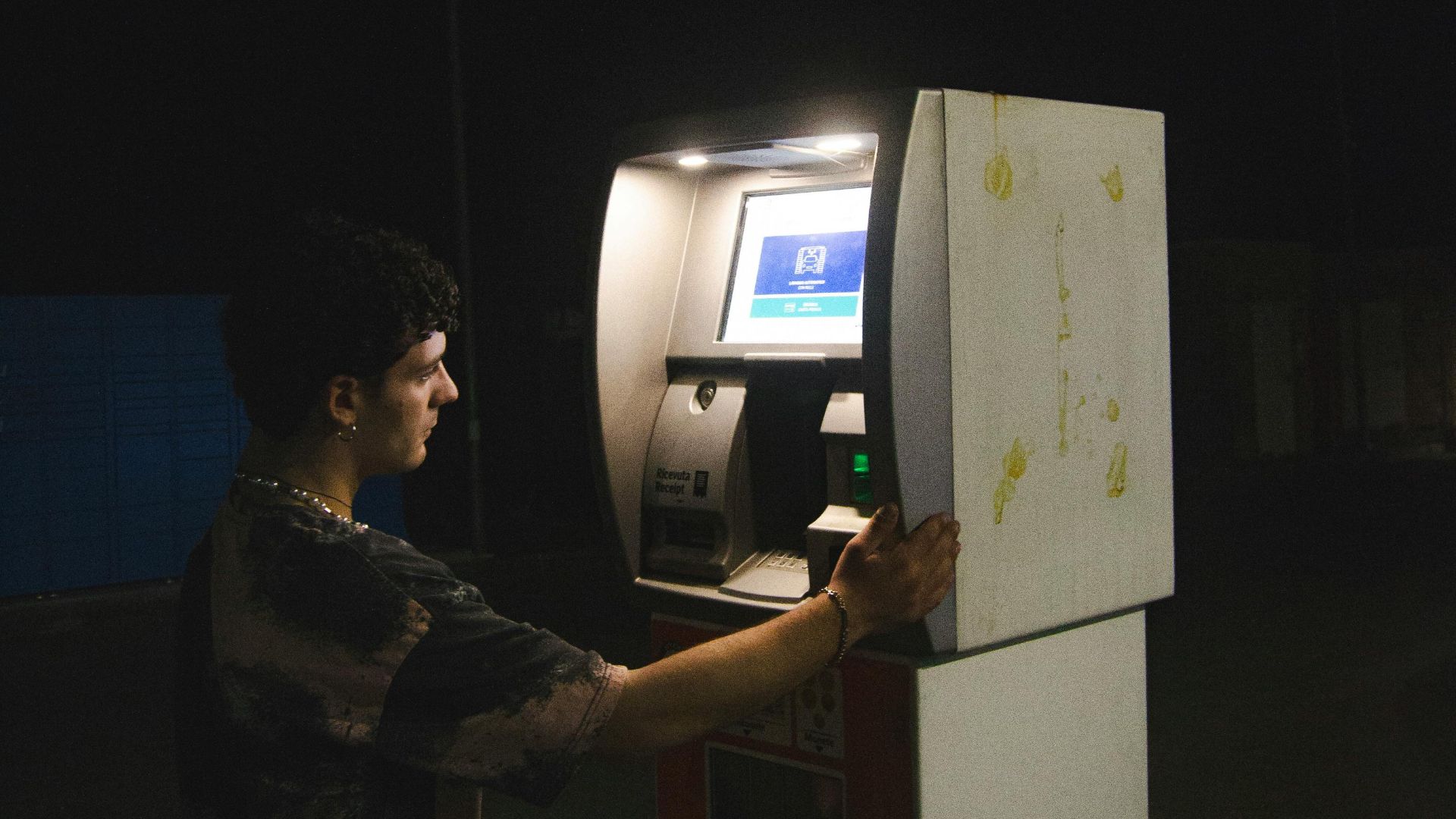 A man uses an ATM on a dimly lit street at night, highlighting finance technology.
