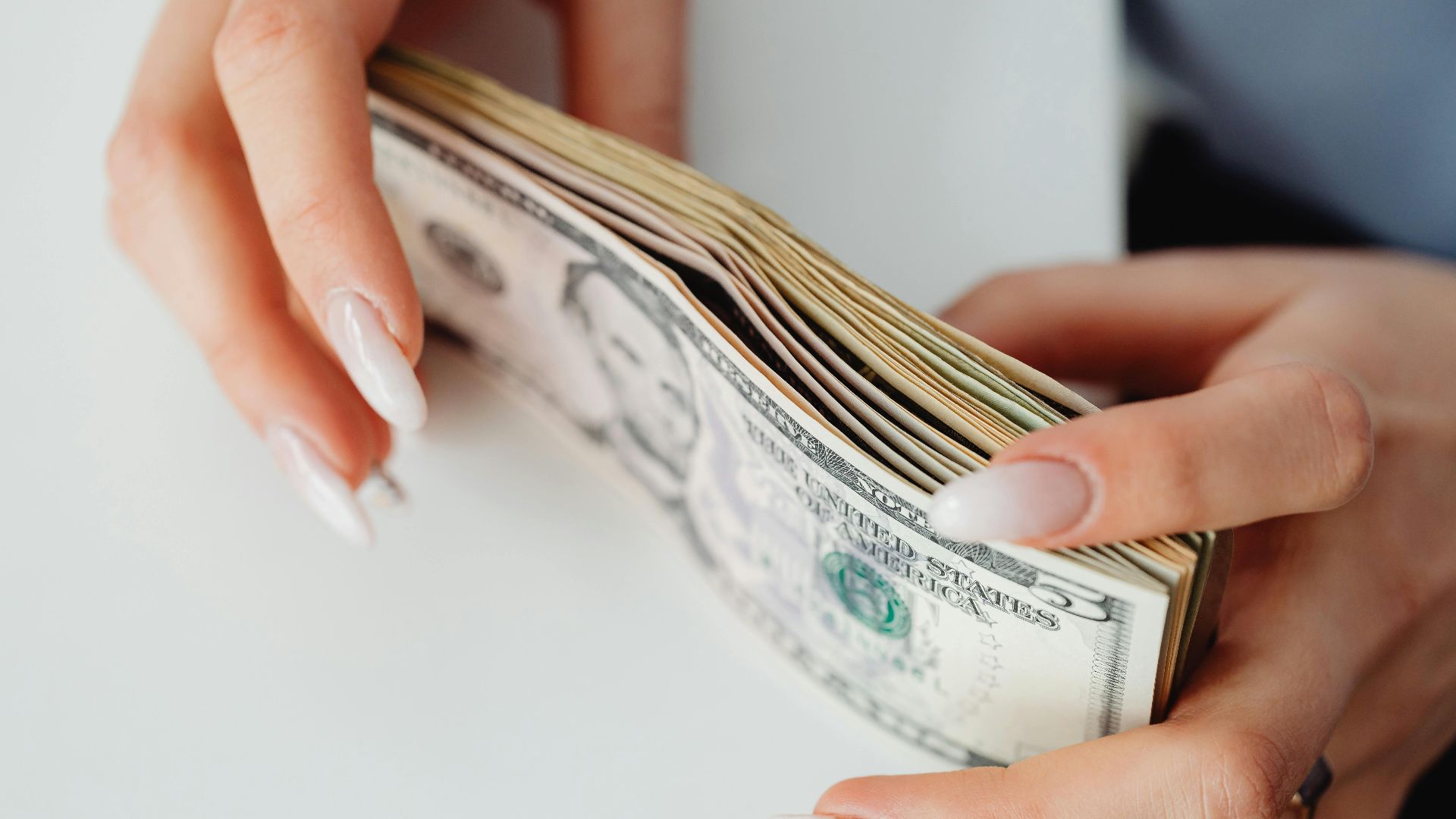 Hands carefully holding a stack of US dollar bills, representing finance and currency.