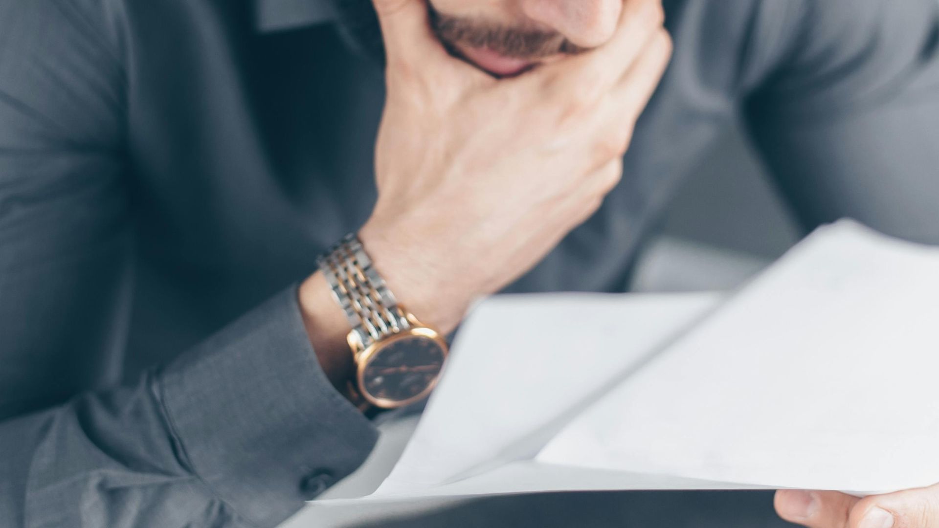 Man in gray shirt with glasses looking concerned over financial papers.